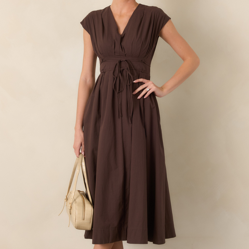 Crop in of a woman in a brown, cap sleeve, brown midi dress with a v-neck and thing string belt at the waist.