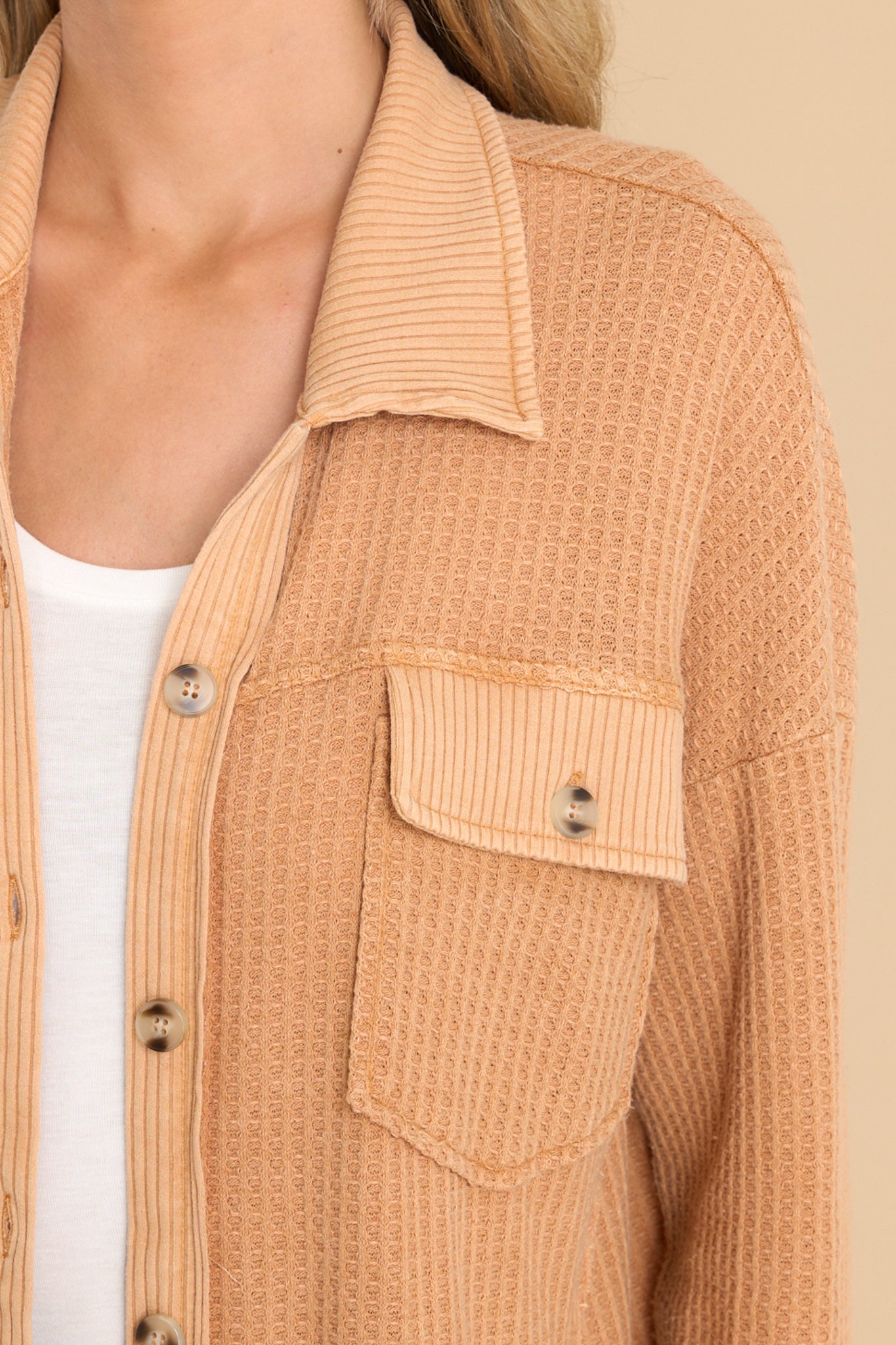 Close up view of this top that features a collared neckline, functional buttons down the front, bust pockets with button closures, long sleeves, and a mixed-textured design throughout.