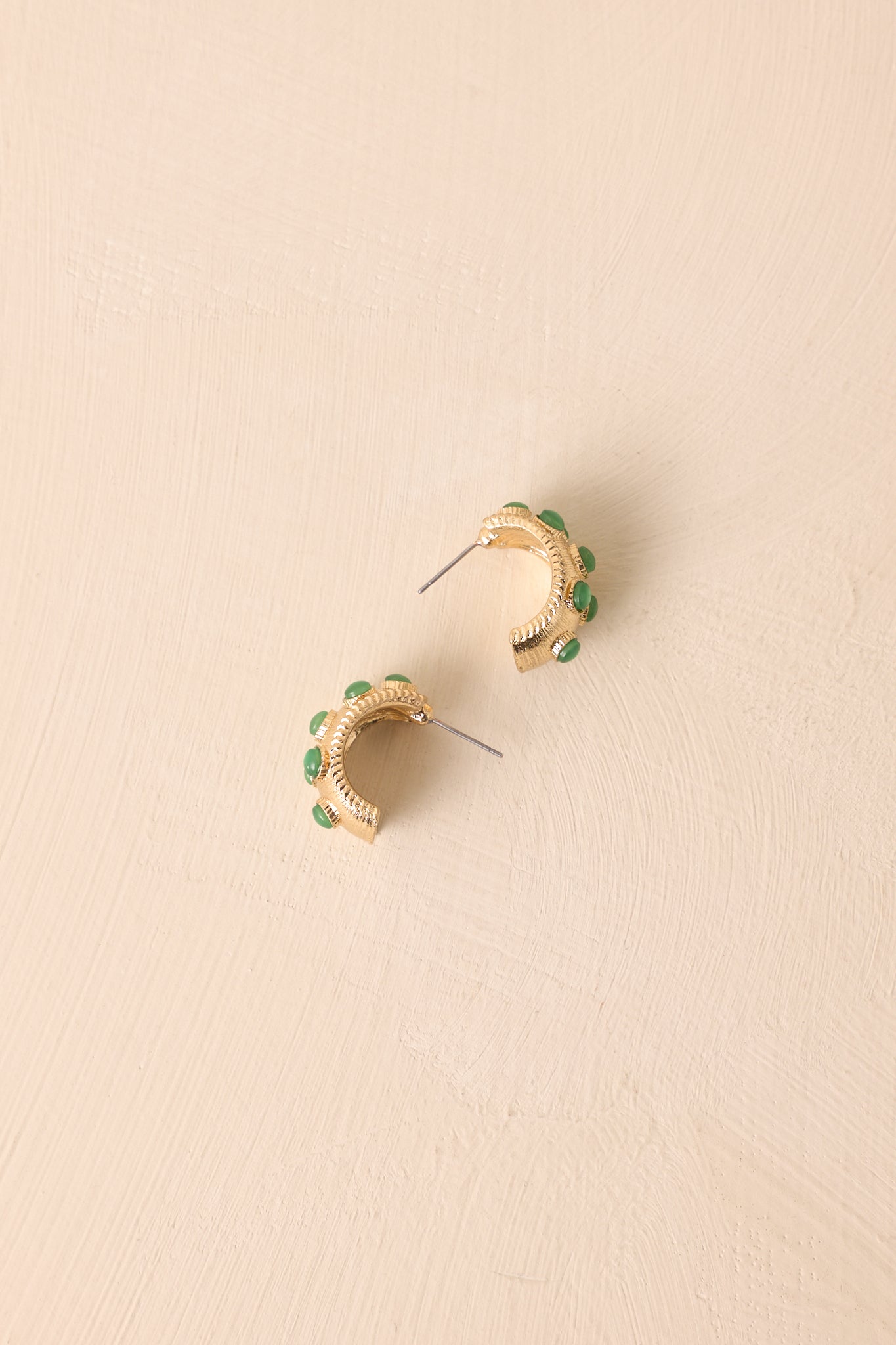 Bezel-set green stone earrings in worn gold with incomplete hoop shape shown on a neutral background.