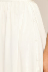 Detailed view of white midi dress that features button detailing down the side of the skirt.