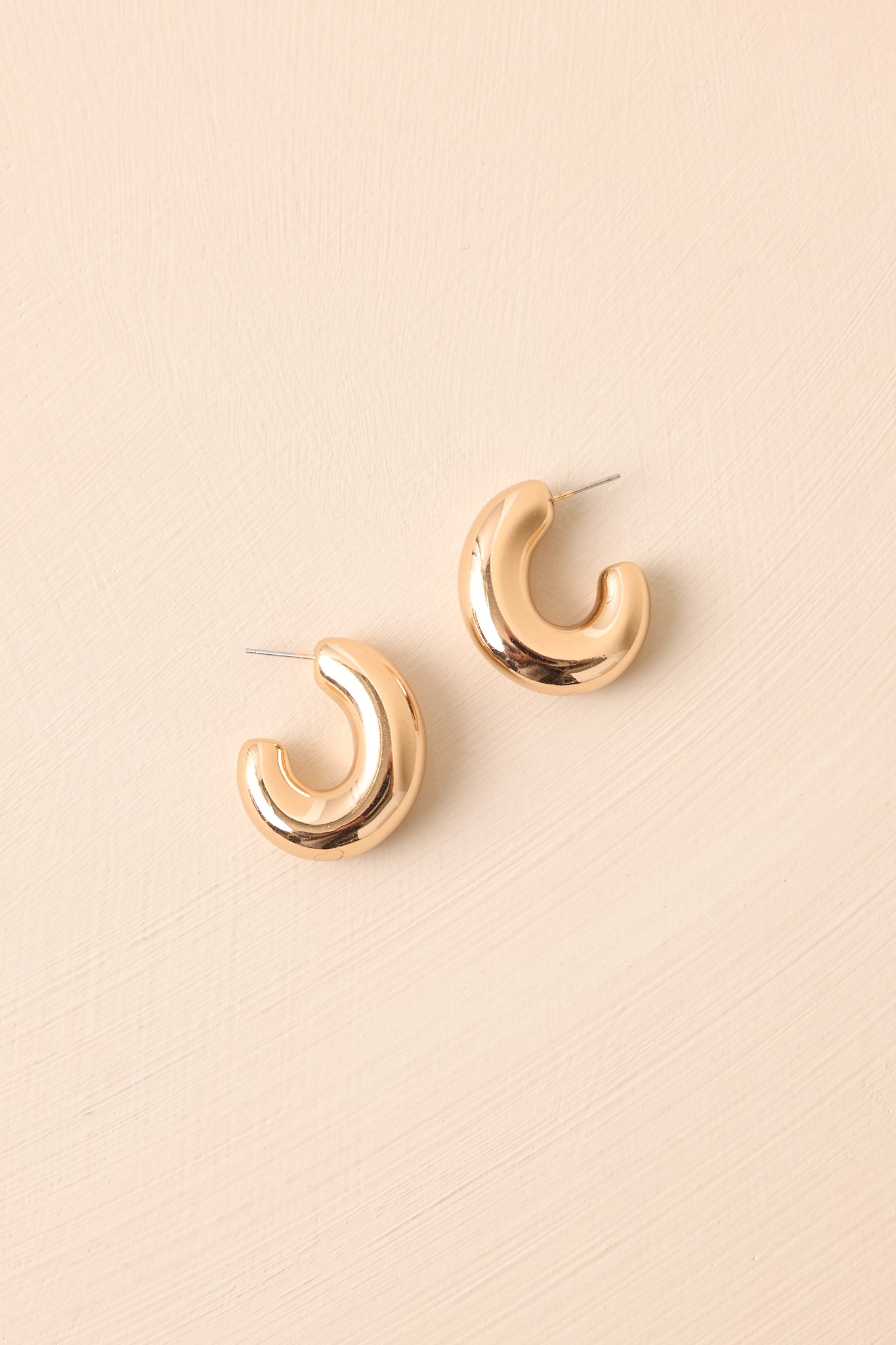 Shiny gold open hoop earrings with a bold dome design resting side by side on beige background.