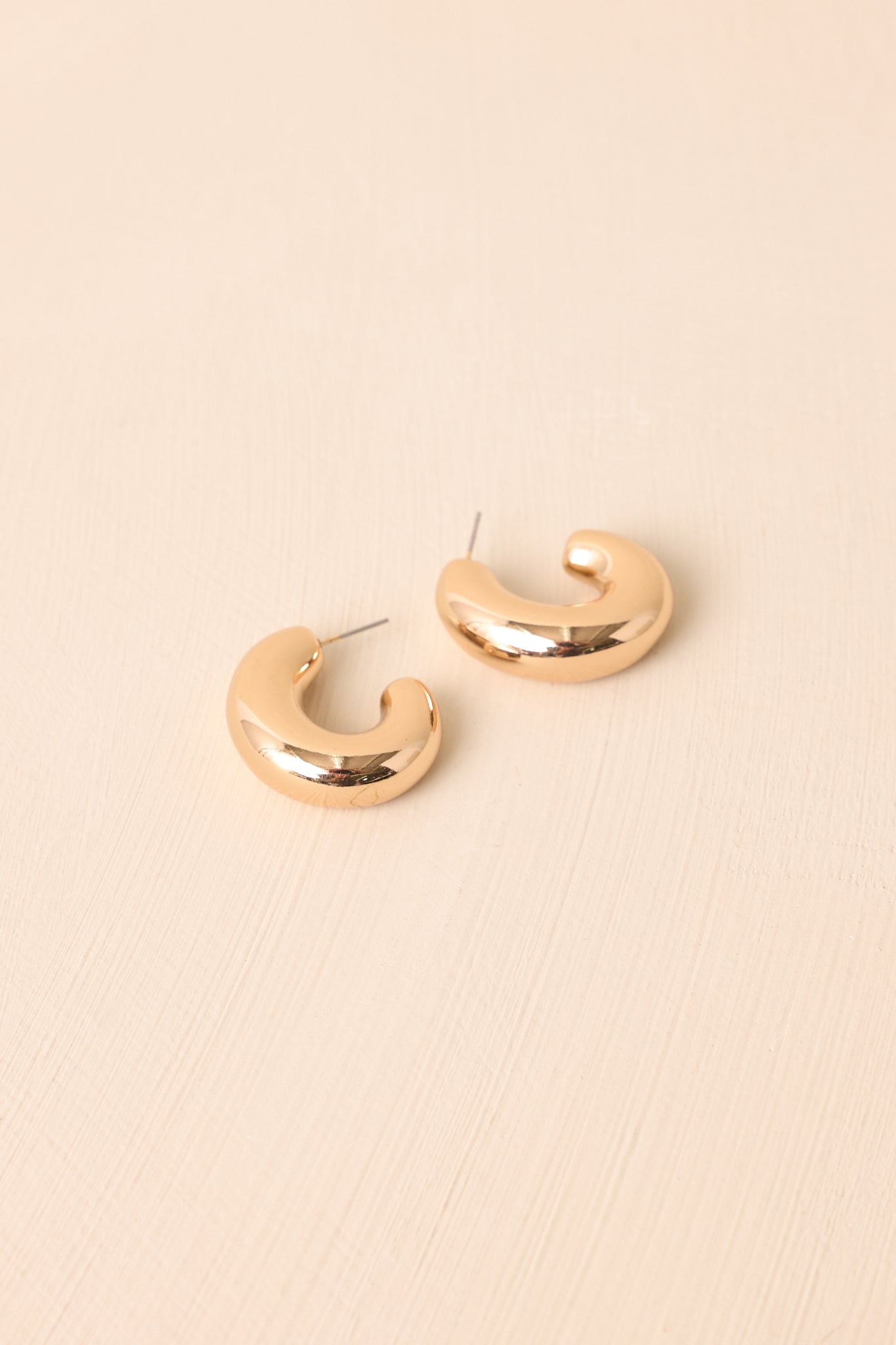 Pair of dome-shaped chunky gold hoop earrings displayed against a beige backdrop.