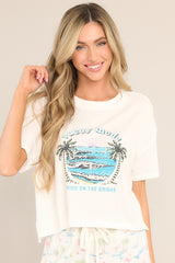 This white tee features a crew neckline, dropped shoulders, a tropical graphic, a slightly cropped length, a split hemline, and short sleeves.