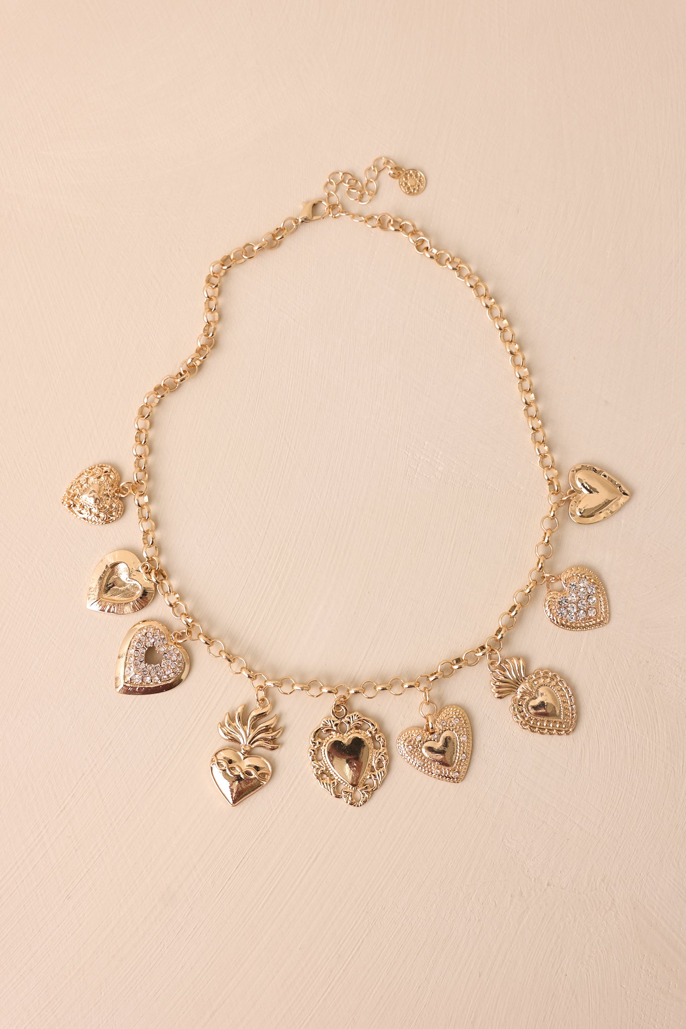 A gold necklace displayed on a beige background, showcasing its delicate circle chain and an array of gold heart charms in different sizes and designs.