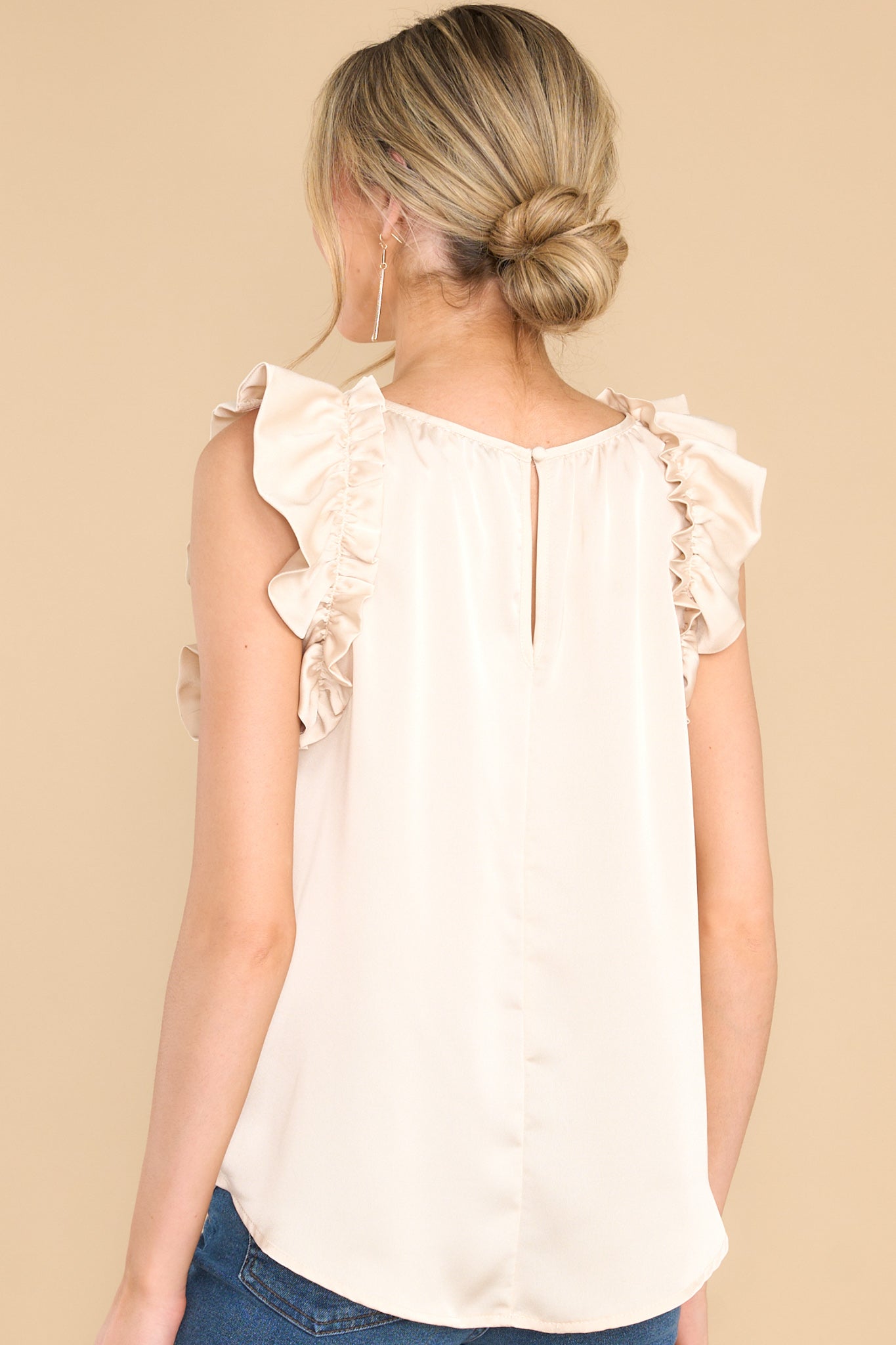Back view of this top that features a ruffled neckline, ruffled sleeves, a satin-like material throughout, and a keyhole button detail in the back.