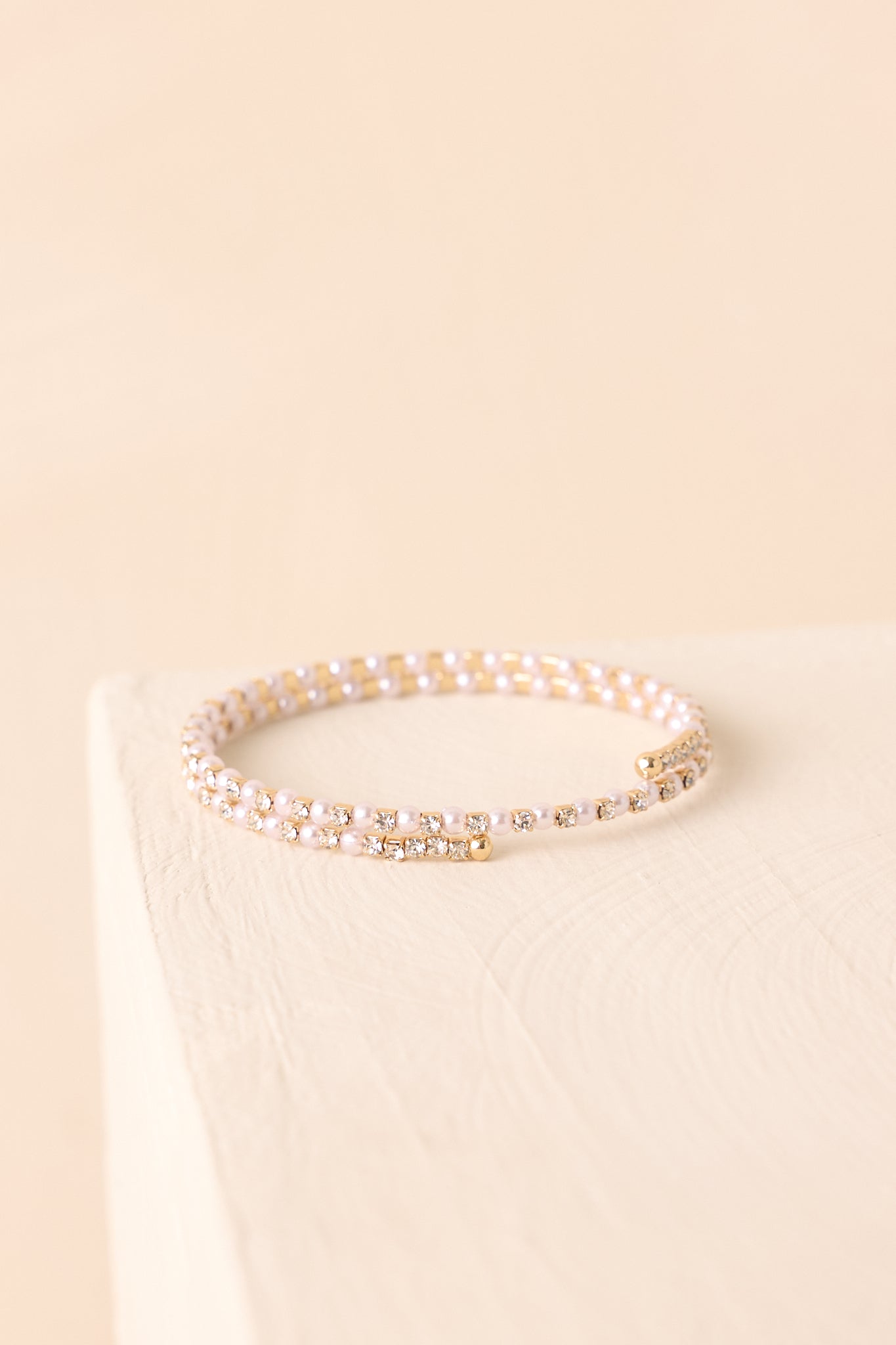A detailed shot of the wrap bracelet focusing on small round faux pearls, clear rhinestones, and gold-tone settings.