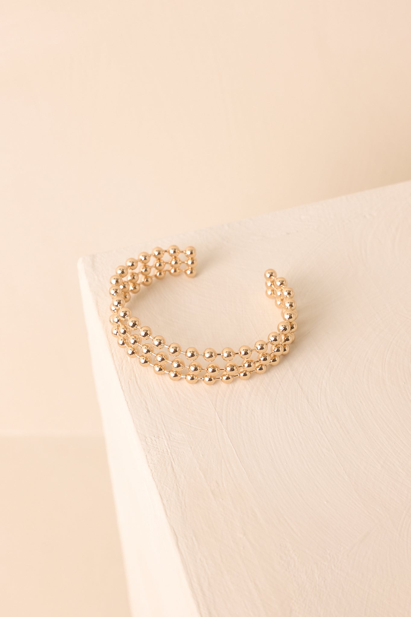 The open-design gold bracelet shown against a beige backdrop with evenly spaced prongs.