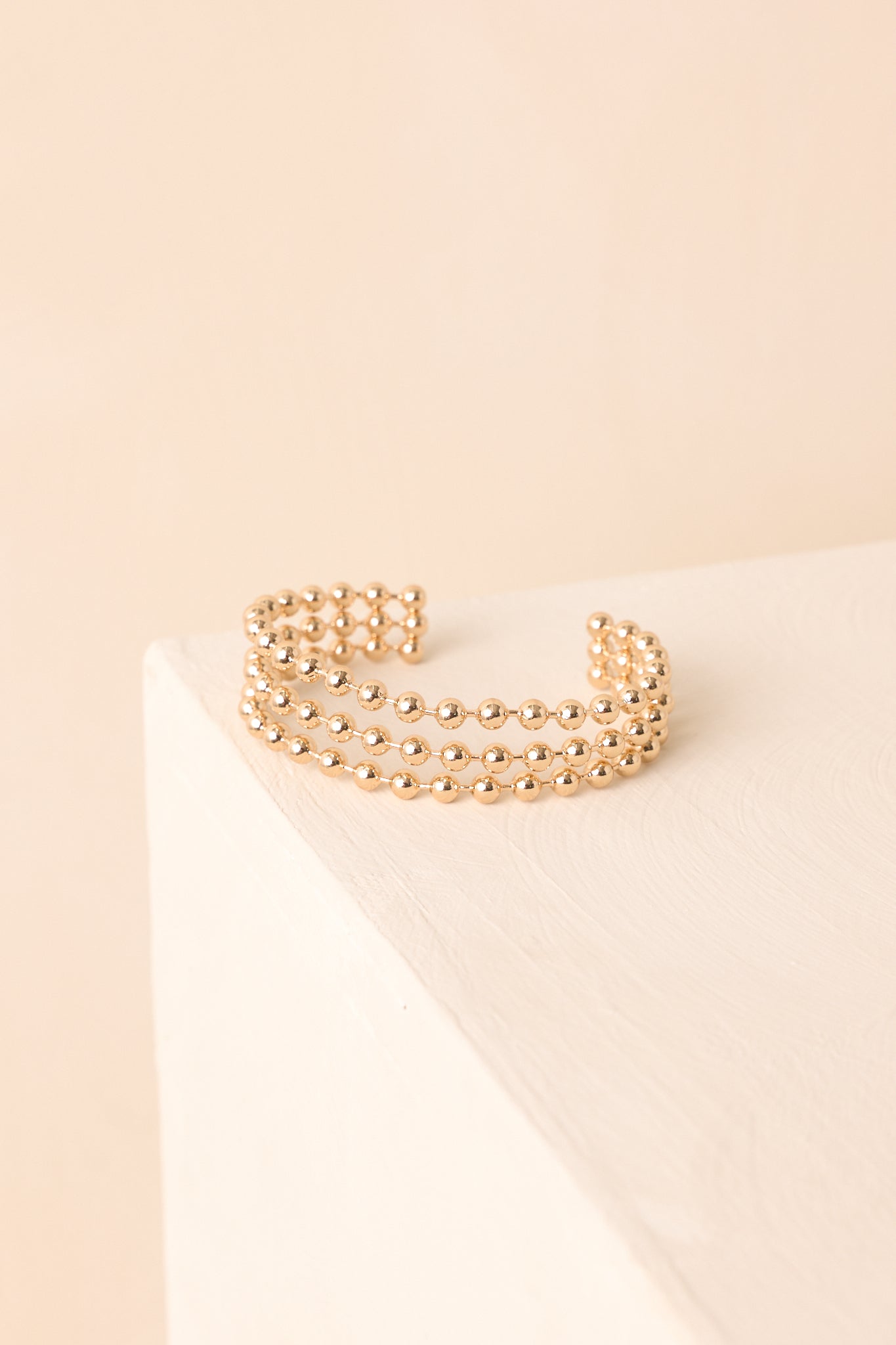 A detailed shot of the gold cuff bracelet showing its smooth band and raised ball prong texture.