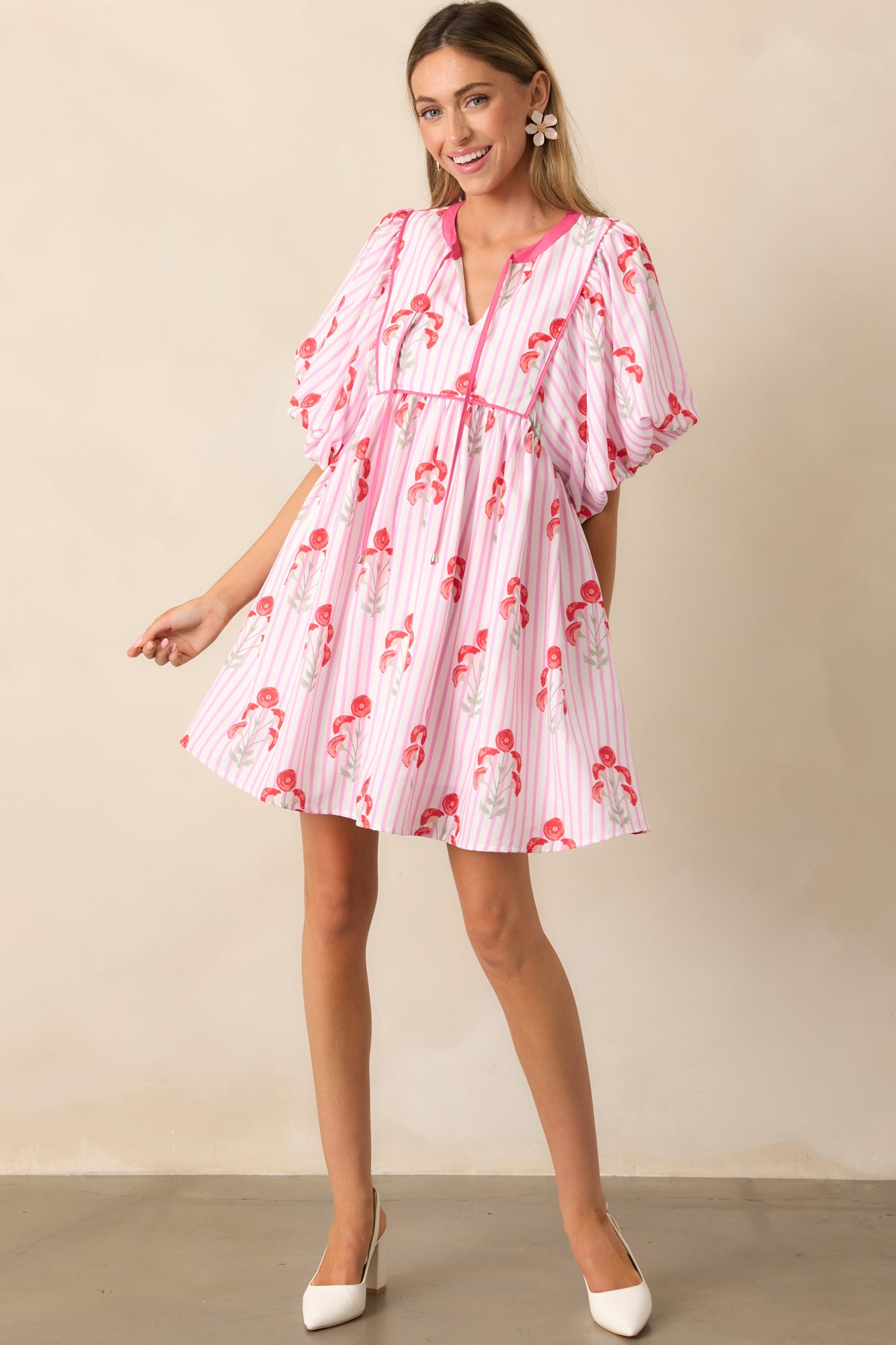 A vibrant pink mini dress with a self-tie notch neckline, puff sleeves, and a combination of a poppy print and stripe pattern for a bold and playful look.