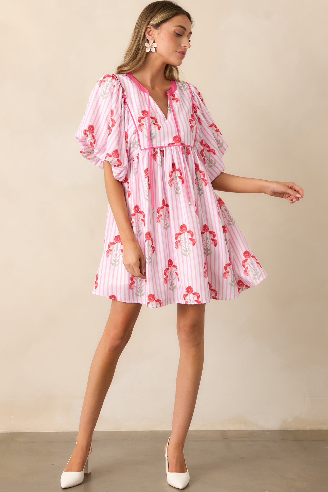 A pink mini dress featuring a notch neckline with a self-tie accent, a relaxed fit, a bold poppy print, a stripe pattern, and puff sleeves.