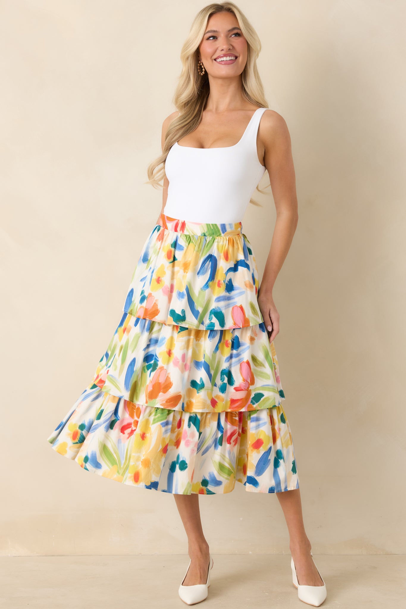 Woman wearing a colorful tiered skirt with a white top on a beige background.