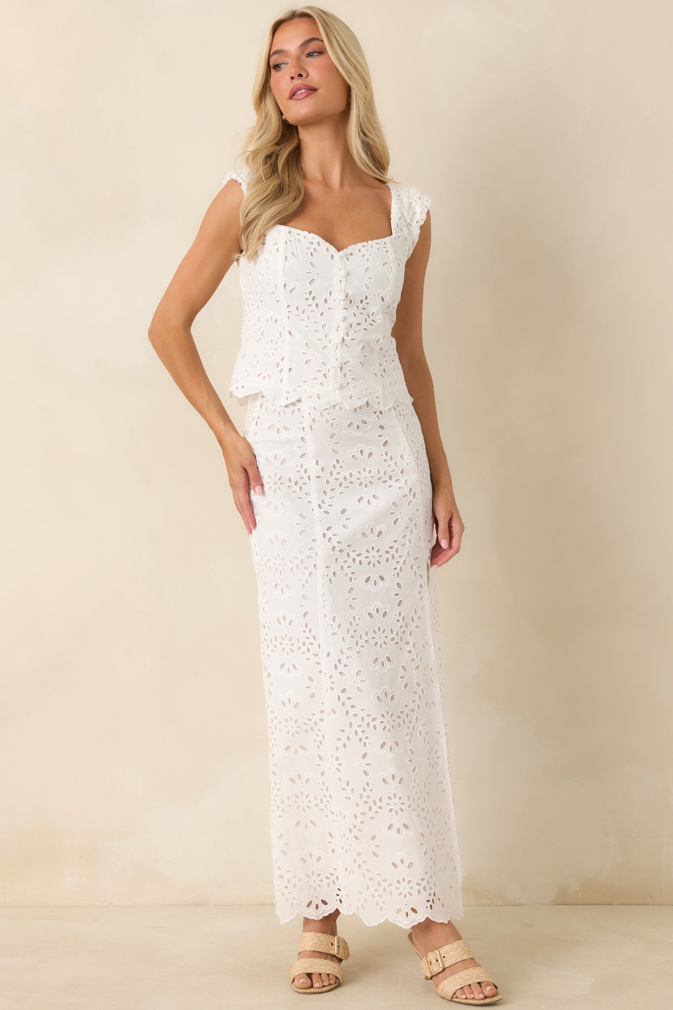 White cotton eyelet top featuring a sweetheart neckline, cap sleeves, floral embroidery, and a fitted silhouette with a scalloped hem.