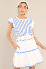 Angled front view of this dress that features a scalloped crew neckline, a striped knitted bodice, a ruffled waistline, functional pockets, scalloped detailing, a scalloped hemline, and ruffled sleeves.