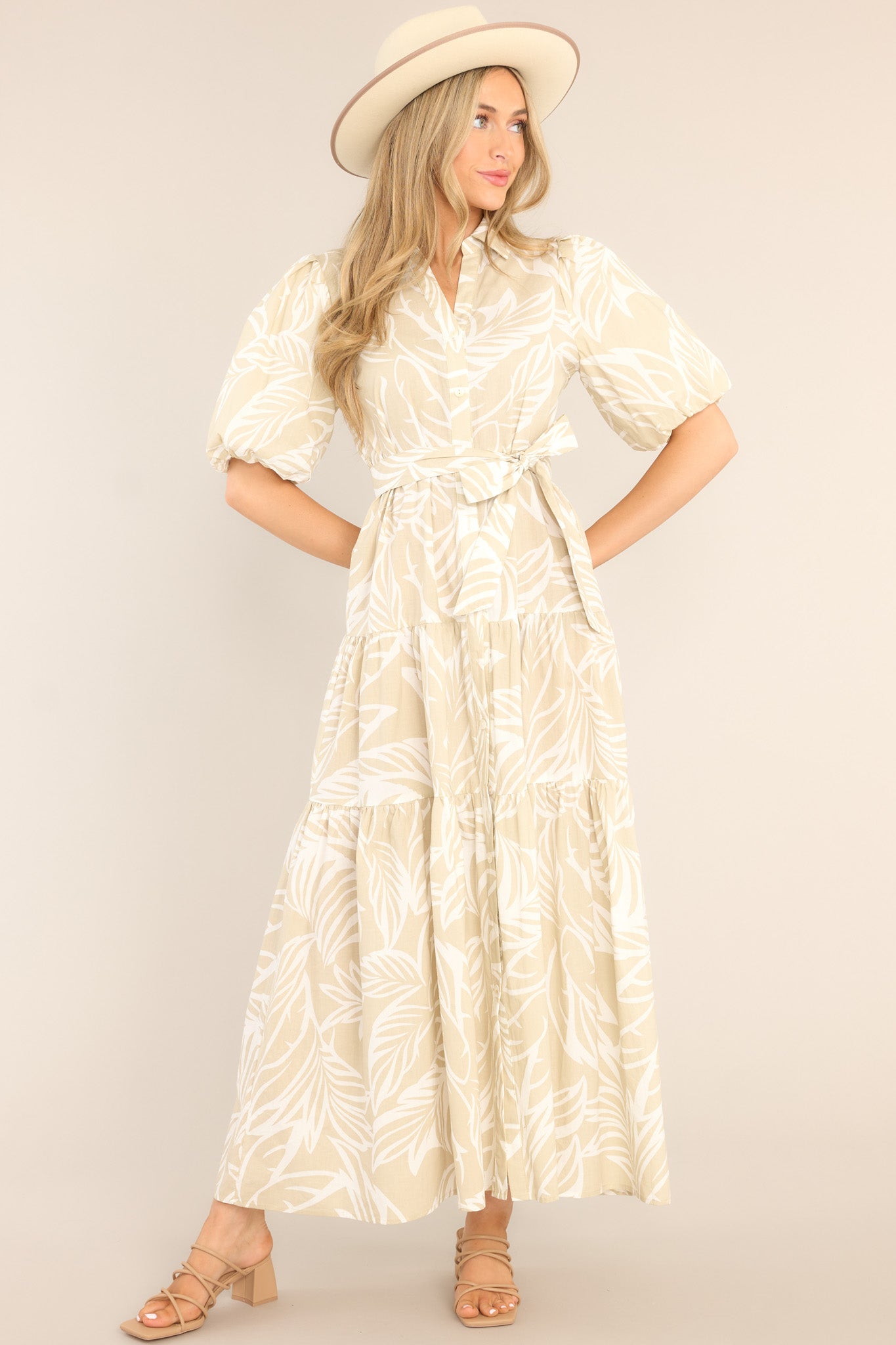 Front view of this dress that features a collared neckline, functional buttons down the front, a self-tie belt, a tiered design, elastic cuffed sleeves, and a tropical palm frond print.