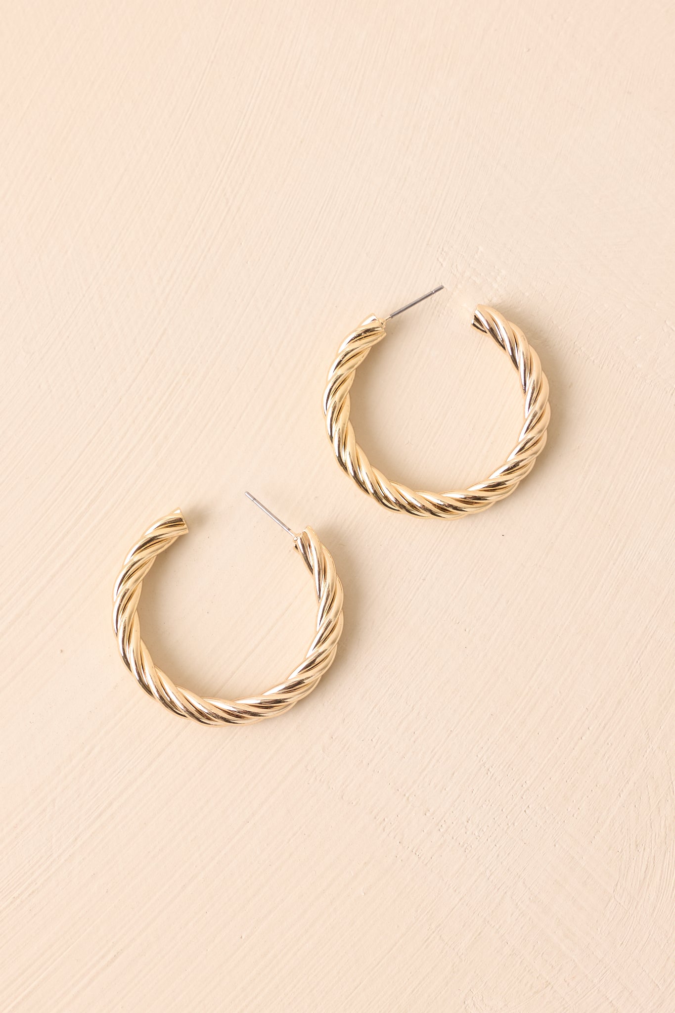 Flat lay of the earrings on a beige surface showing the dimensional rope twist and high-shine finish.