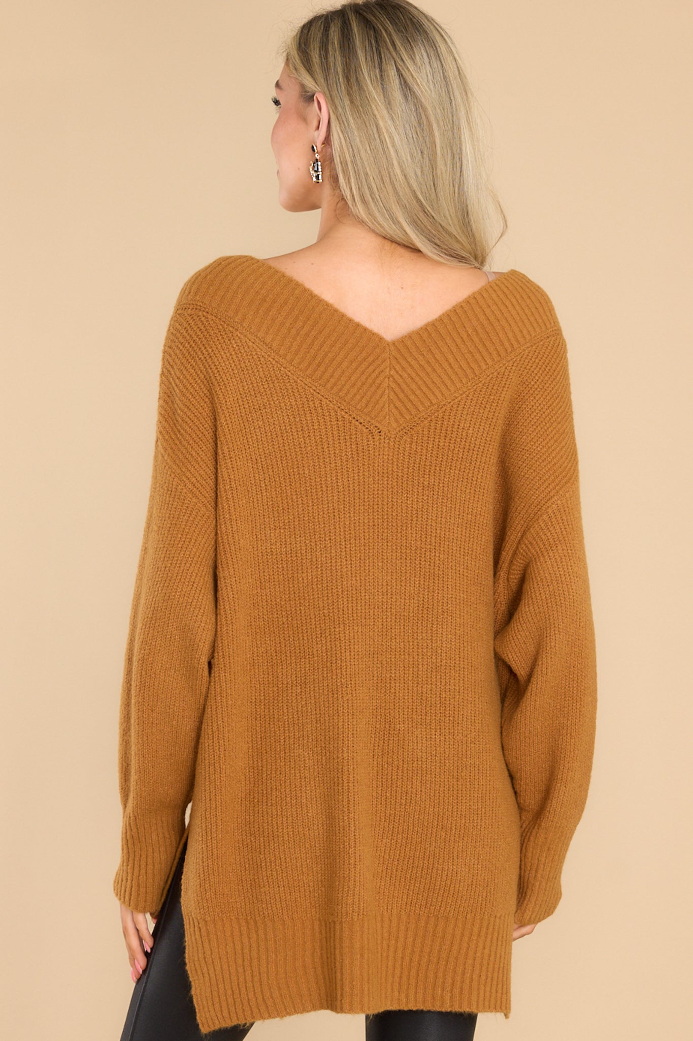 Back view of this sweater that features a wide v-neckline, long sleeves with ribbed cuffs, a bottom hem that is longer in the back and has small slits up both sides, and a super soft feel throughout.