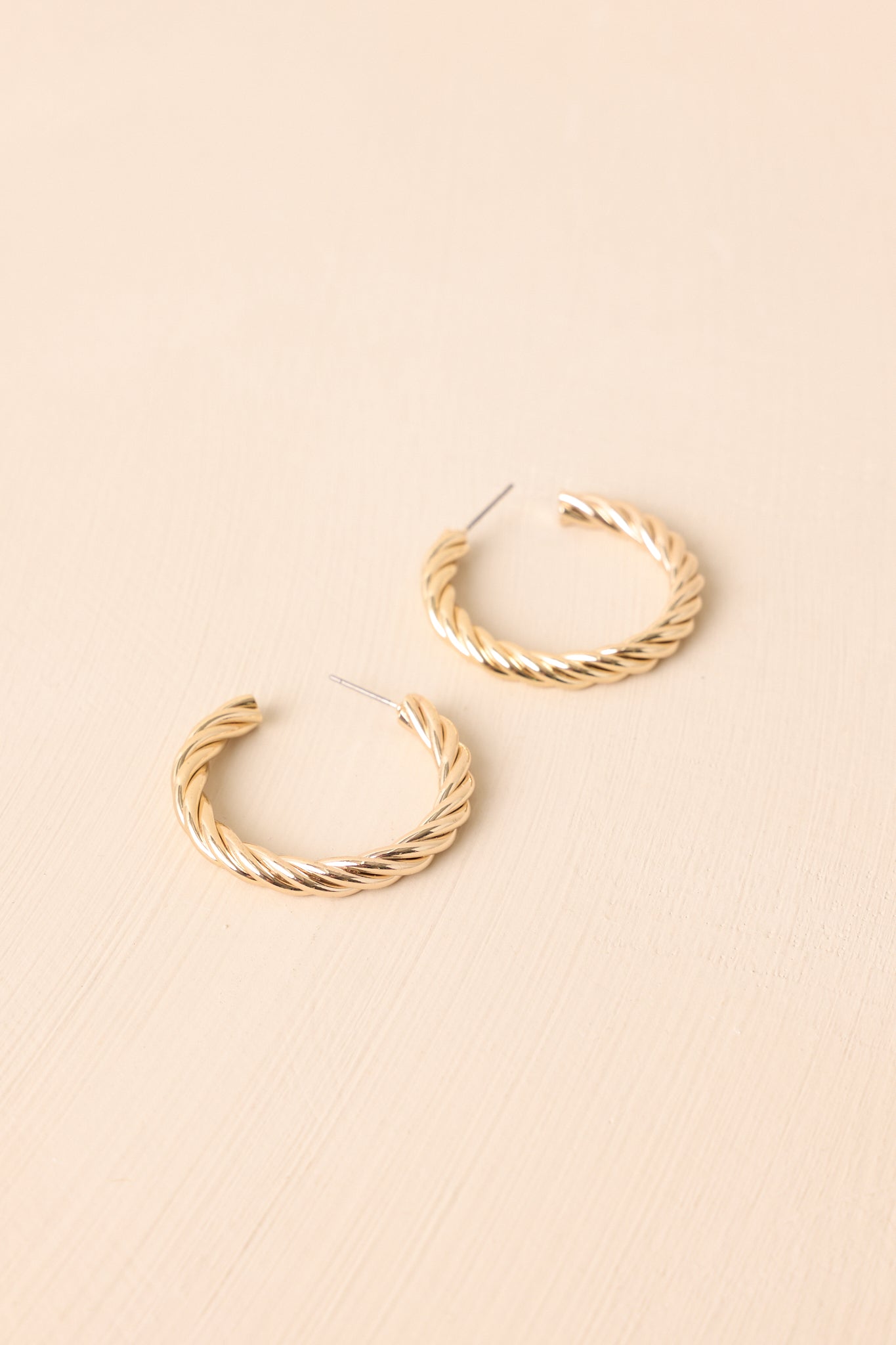 Chunky gold-tone rope earrings displayed on a beige background, emphasizing the bold twisted design and rounded hoops.