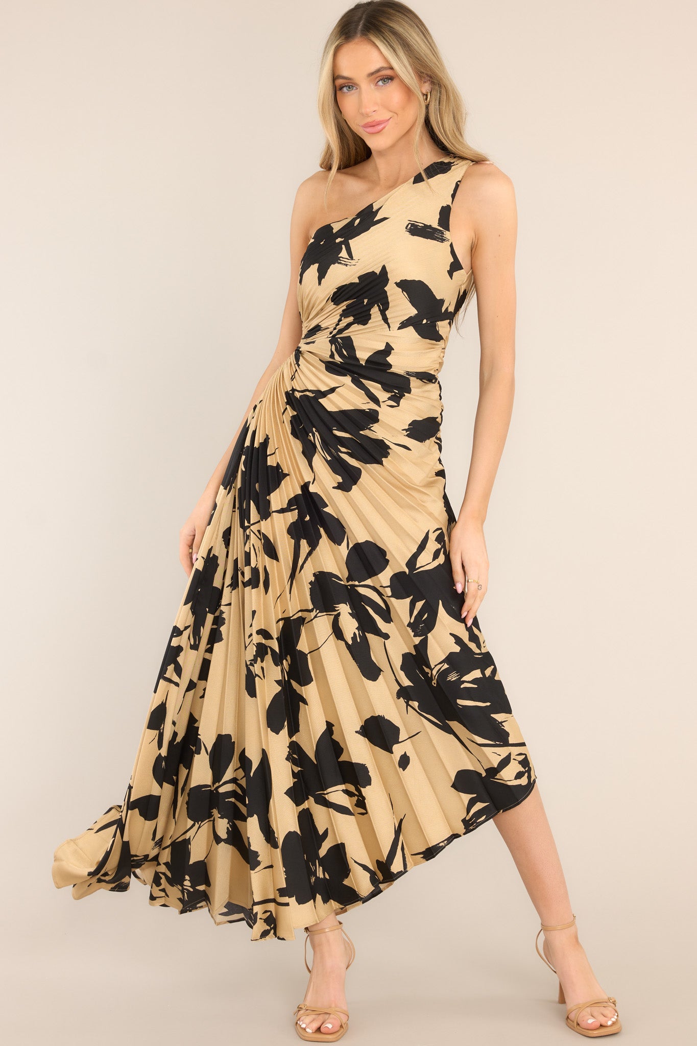 Full body view of this dress that features an asymmetrical neckline, a side zipper, a circular waist cutout, pleats throughout, and a high-low hemline.