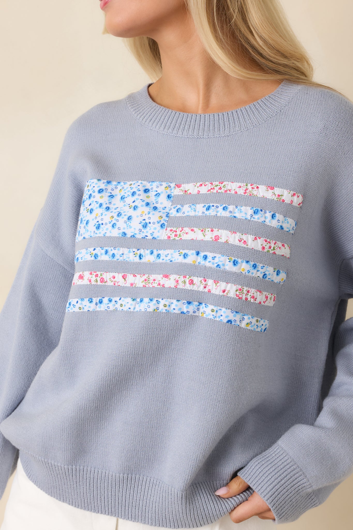 Close-up of floral patchwork American flag detail, showcasing textured embroidery on dusty blue knit.