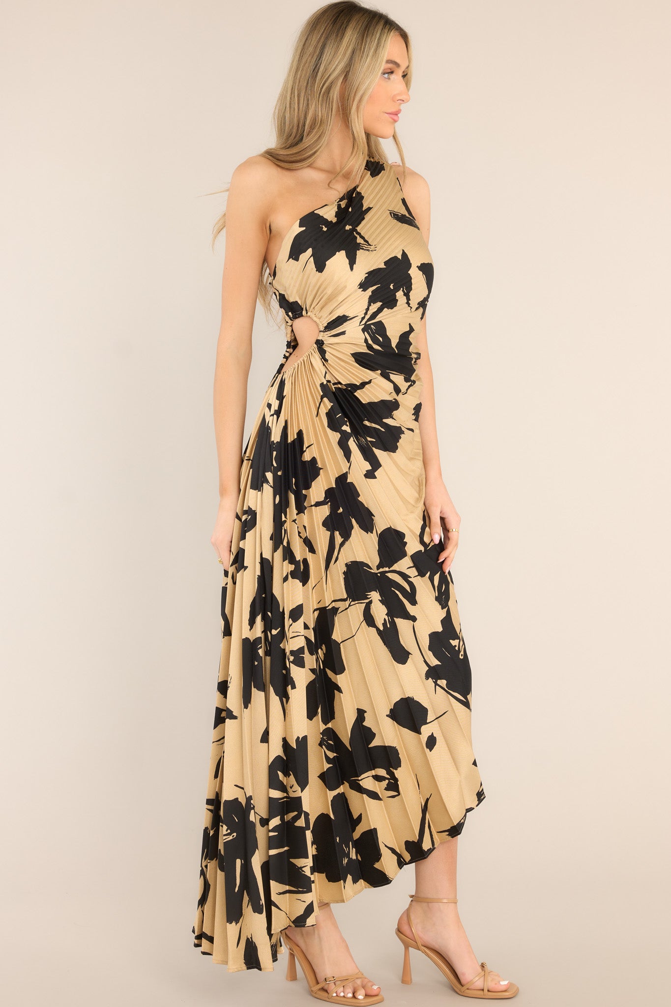 Side view of this dress that features an asymmetrical neckline, a side zipper, a circular waist cutout, pleats throughout, and a high-low hemline.