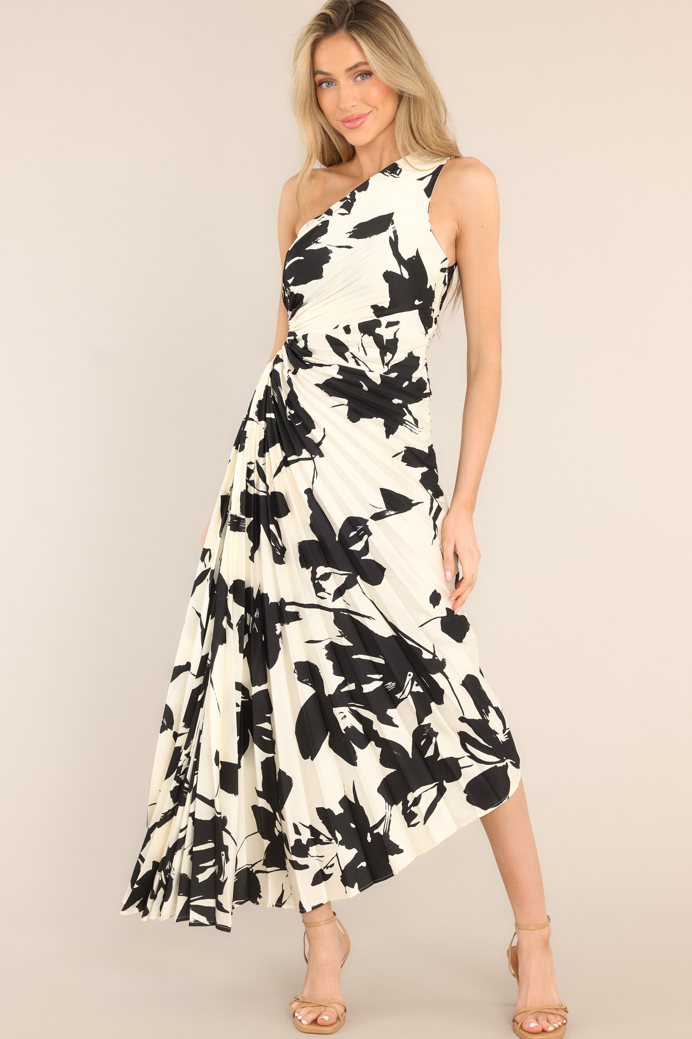 This black and ivory dress features an asymmetrical neckline, a side zipper, a circular waist cutout, pleats throughout, and a high-low hemline.