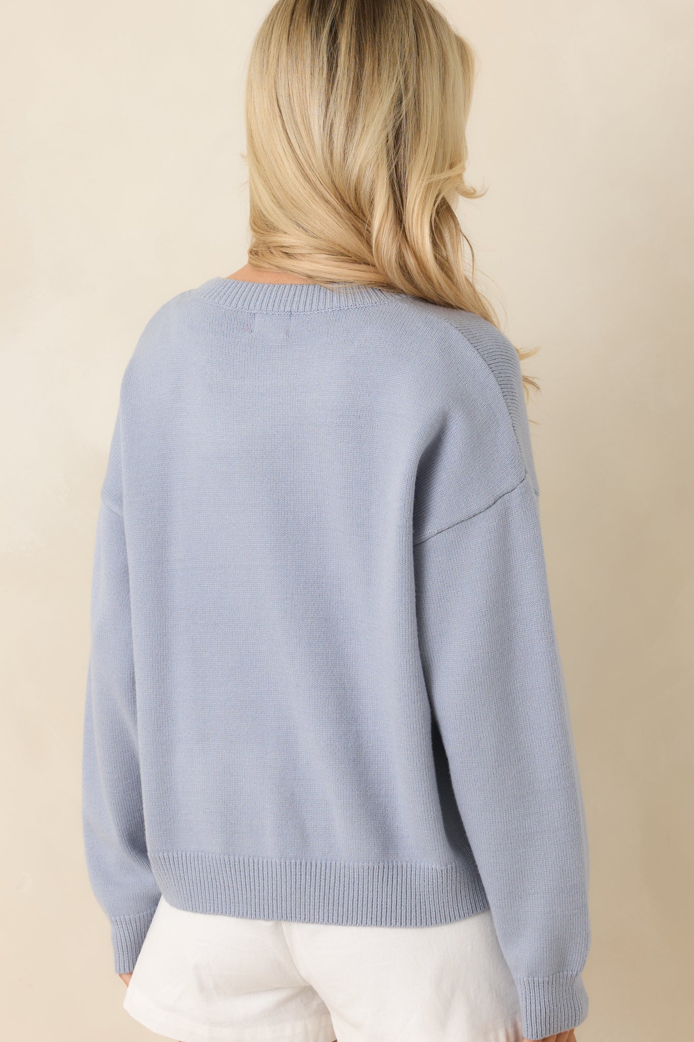 Rear view of dusty blue knit sweater showing smooth fabric, long sleeves, and clean ribbed trim at hem and cuffs.