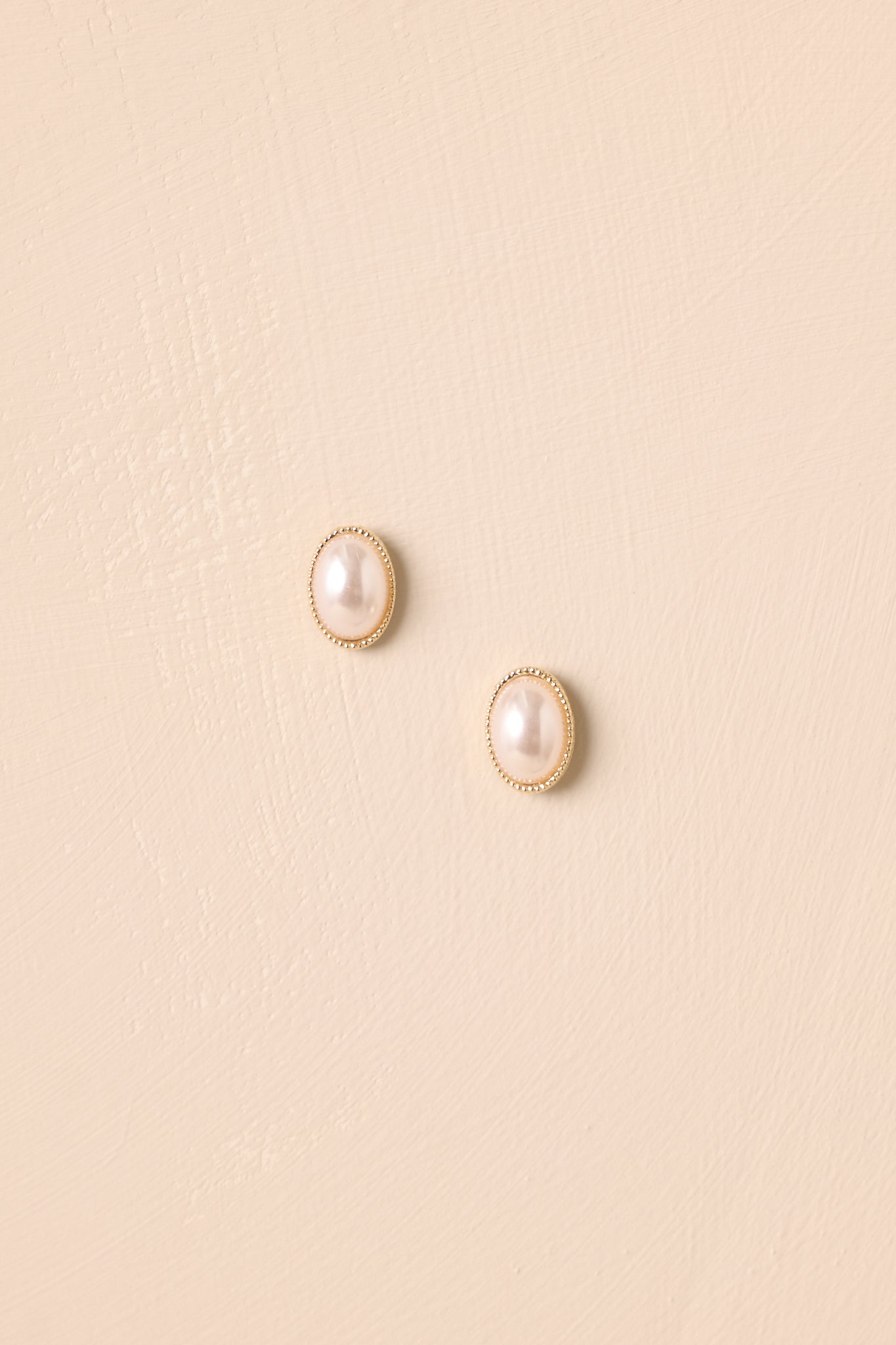 Cropped close-up highlighting the textured gold setting and smooth oval pearls.