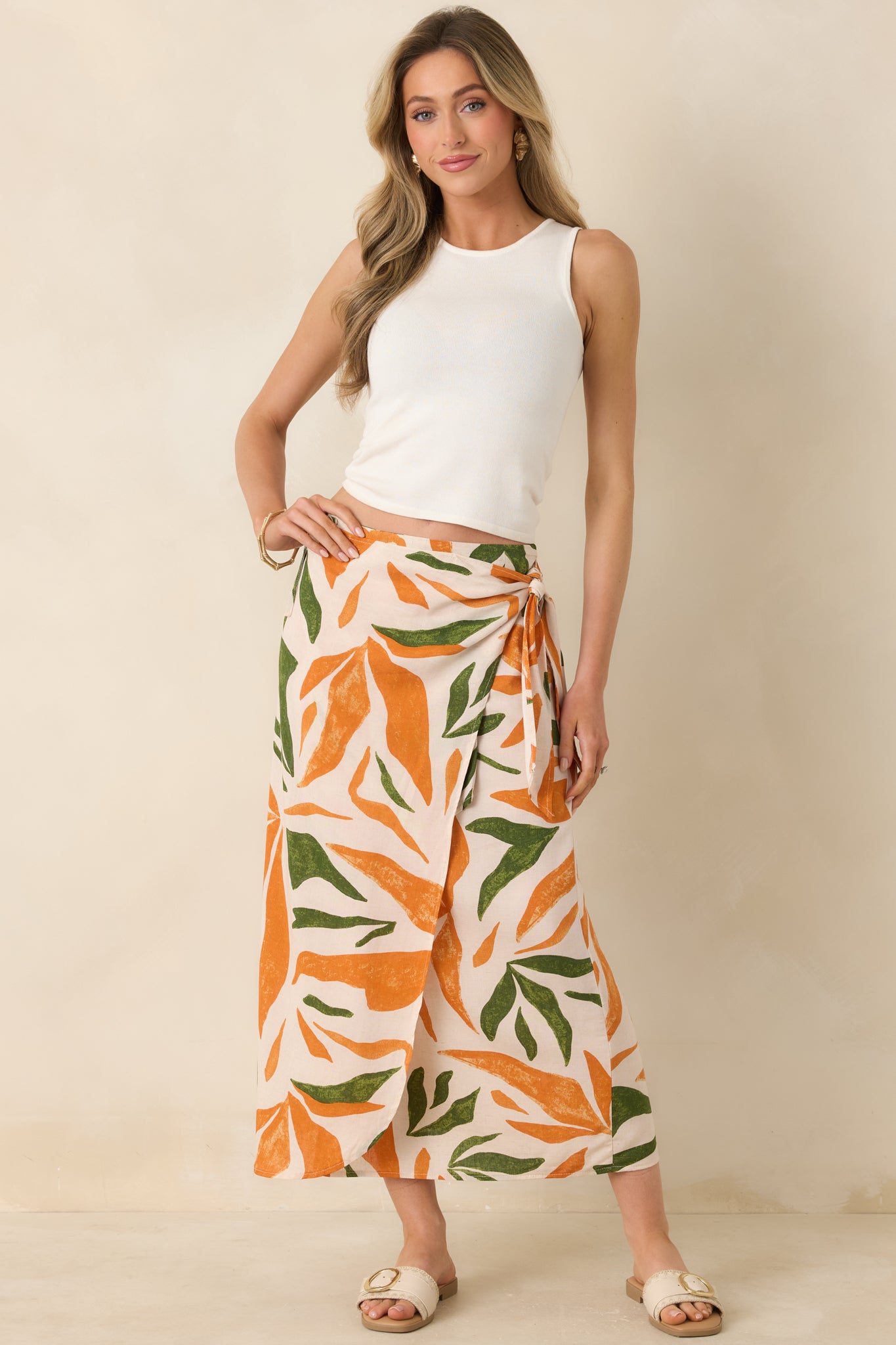 Woman wearing a white sleeveless top and leaf-patterned skirt on a beige background.