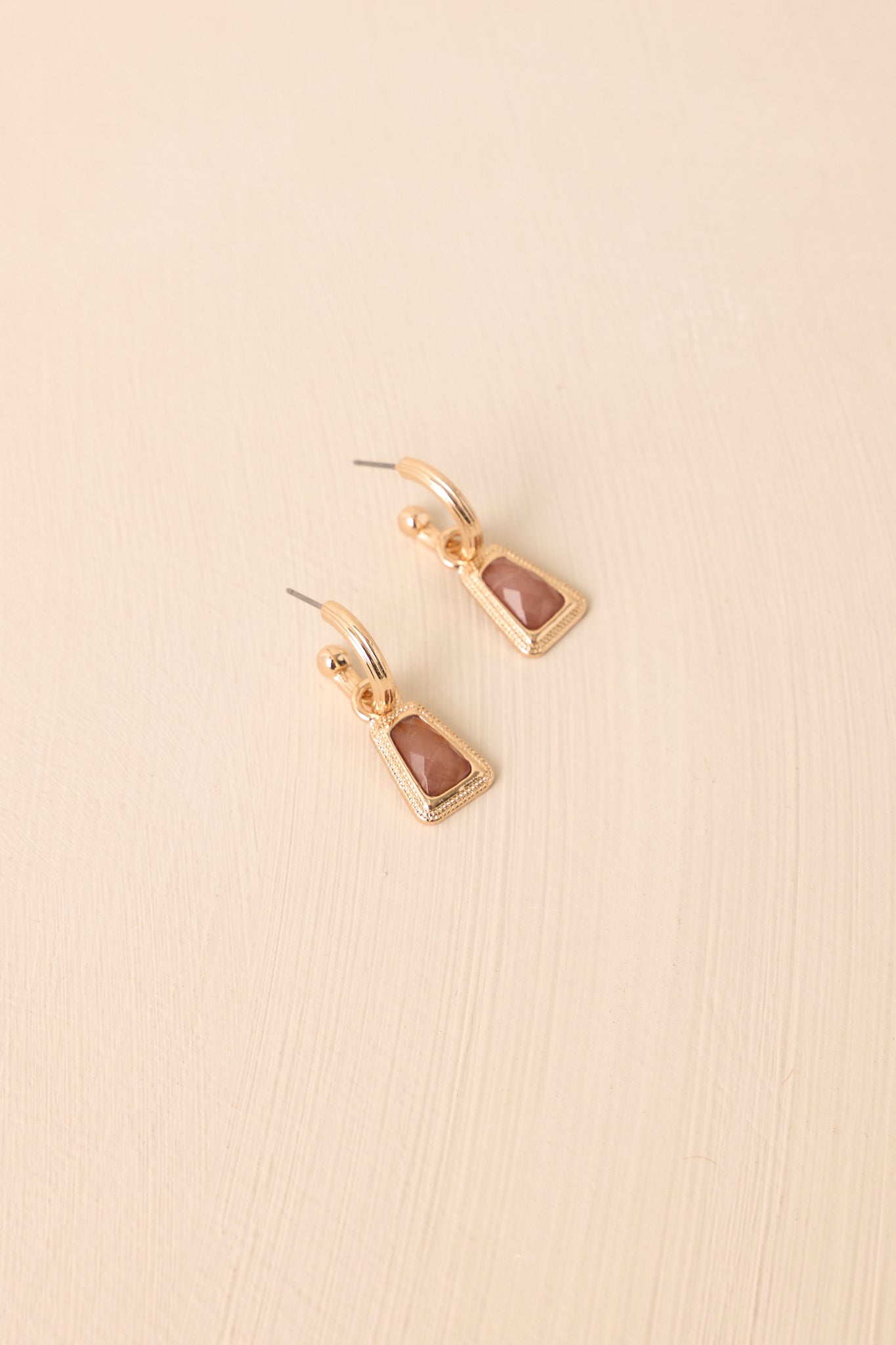 Brown stone drop earrings displayed against a beige background, showing the geometric gold setting and secure clasp design.