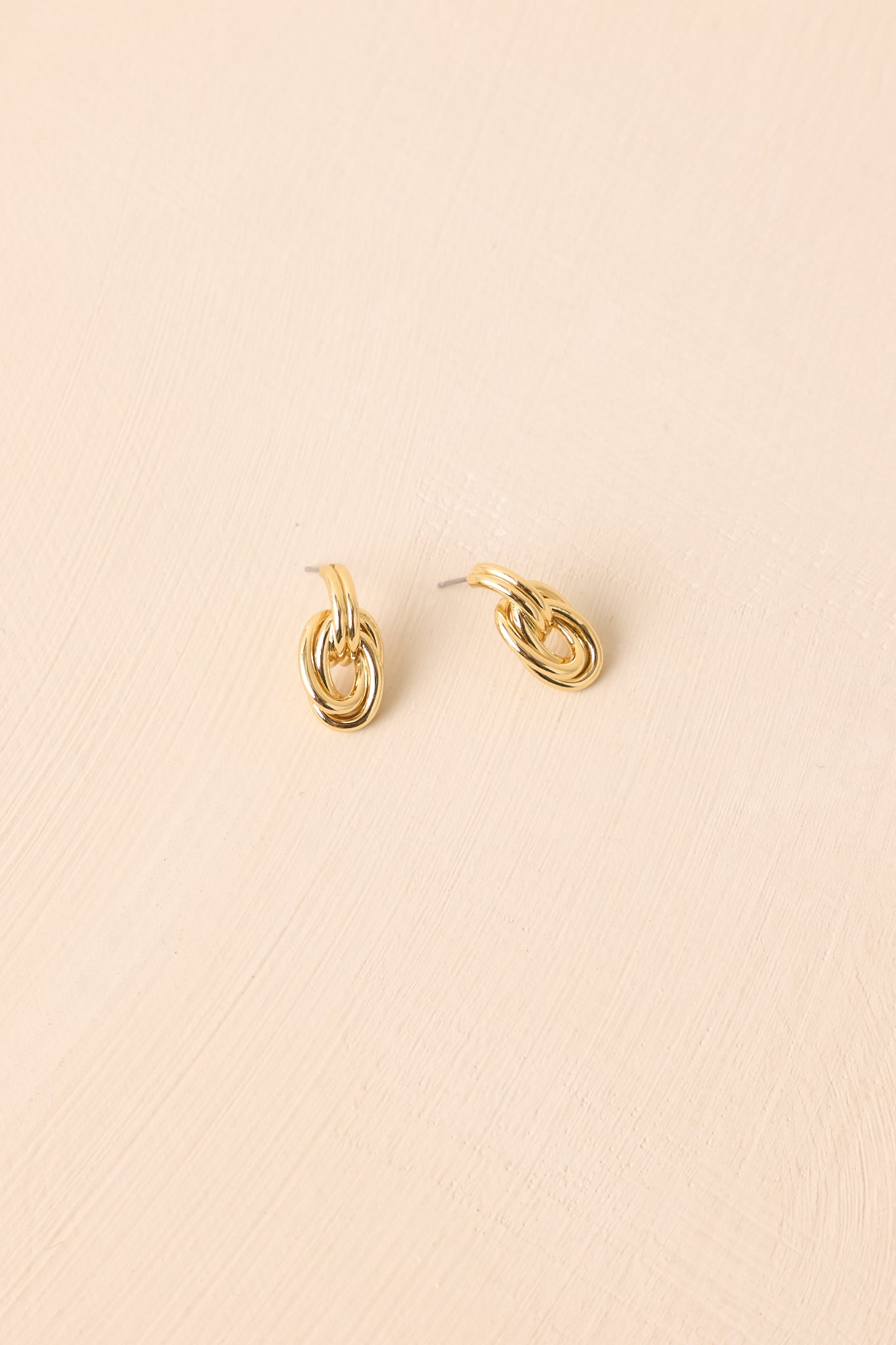 Flat lay of the earrings on a beige surface emphasizing the multiple hoop layers and polished finish.