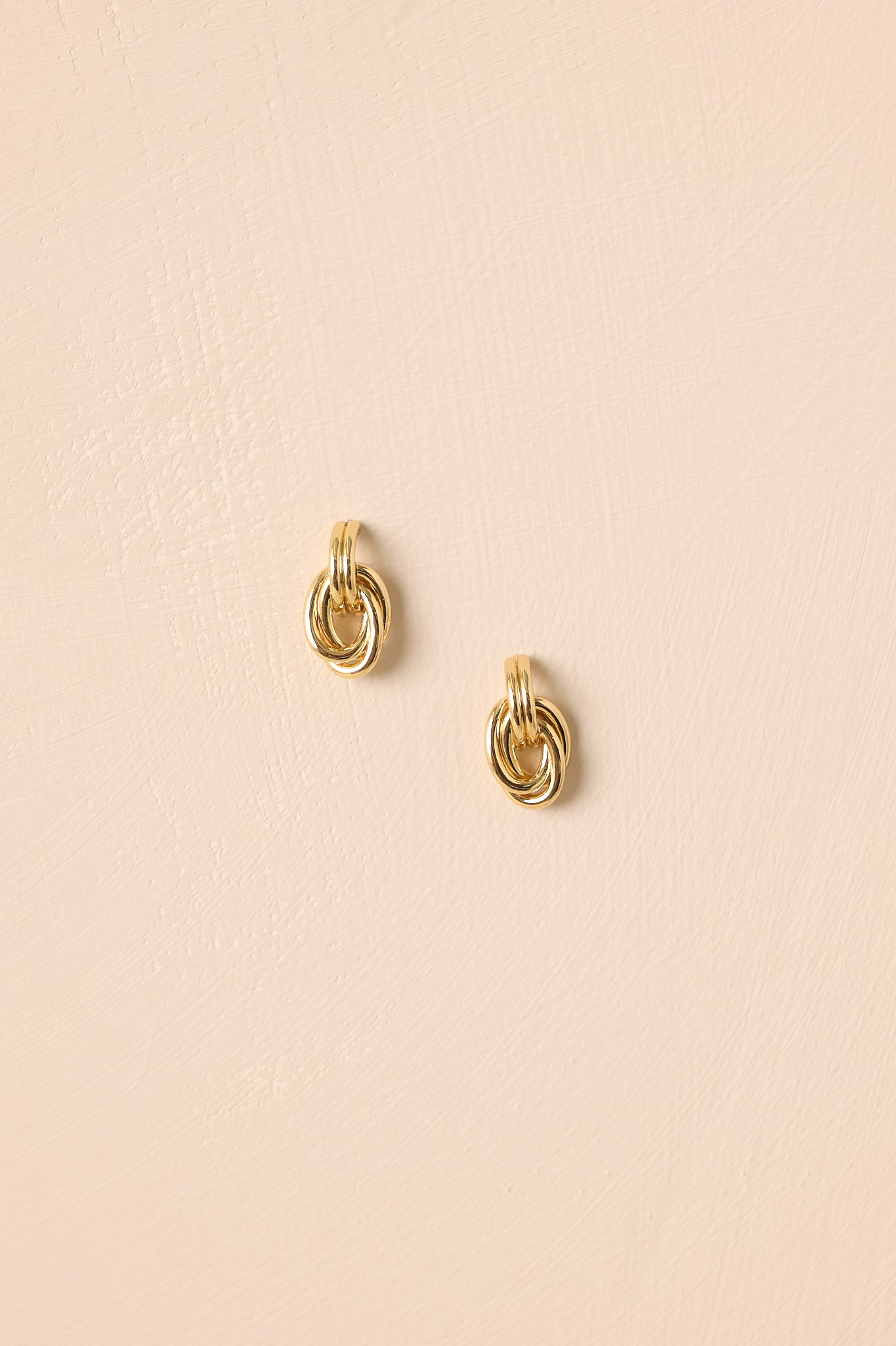 Layered interlocking gold-colored hoop earrings displayed against a beige background.