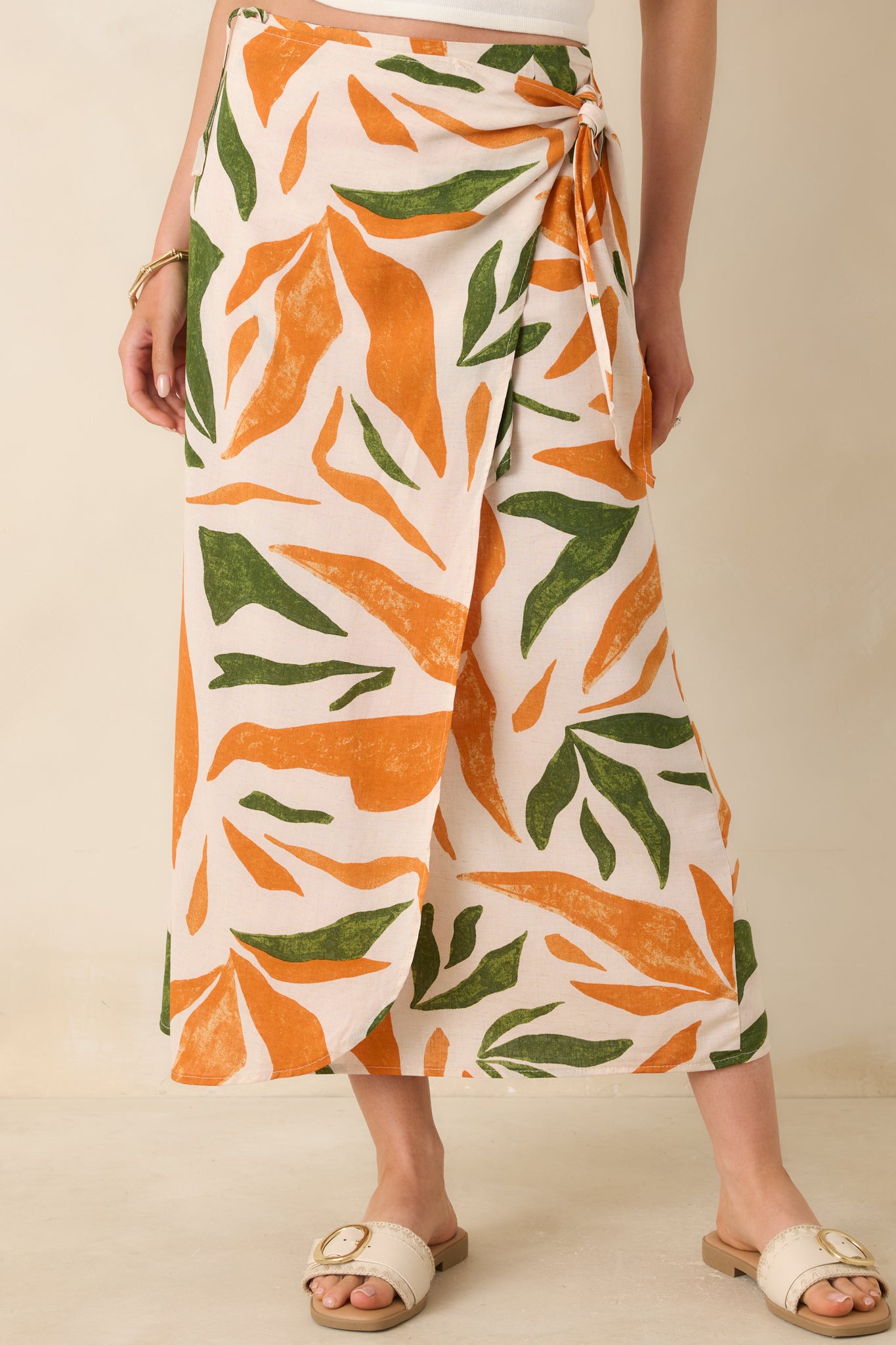 Close up view of this tropical print midi skirt that features a high waisted design, an elastic waist insert, self-tie wrap features, an orange & green tropical print, and a lightweight fabric.