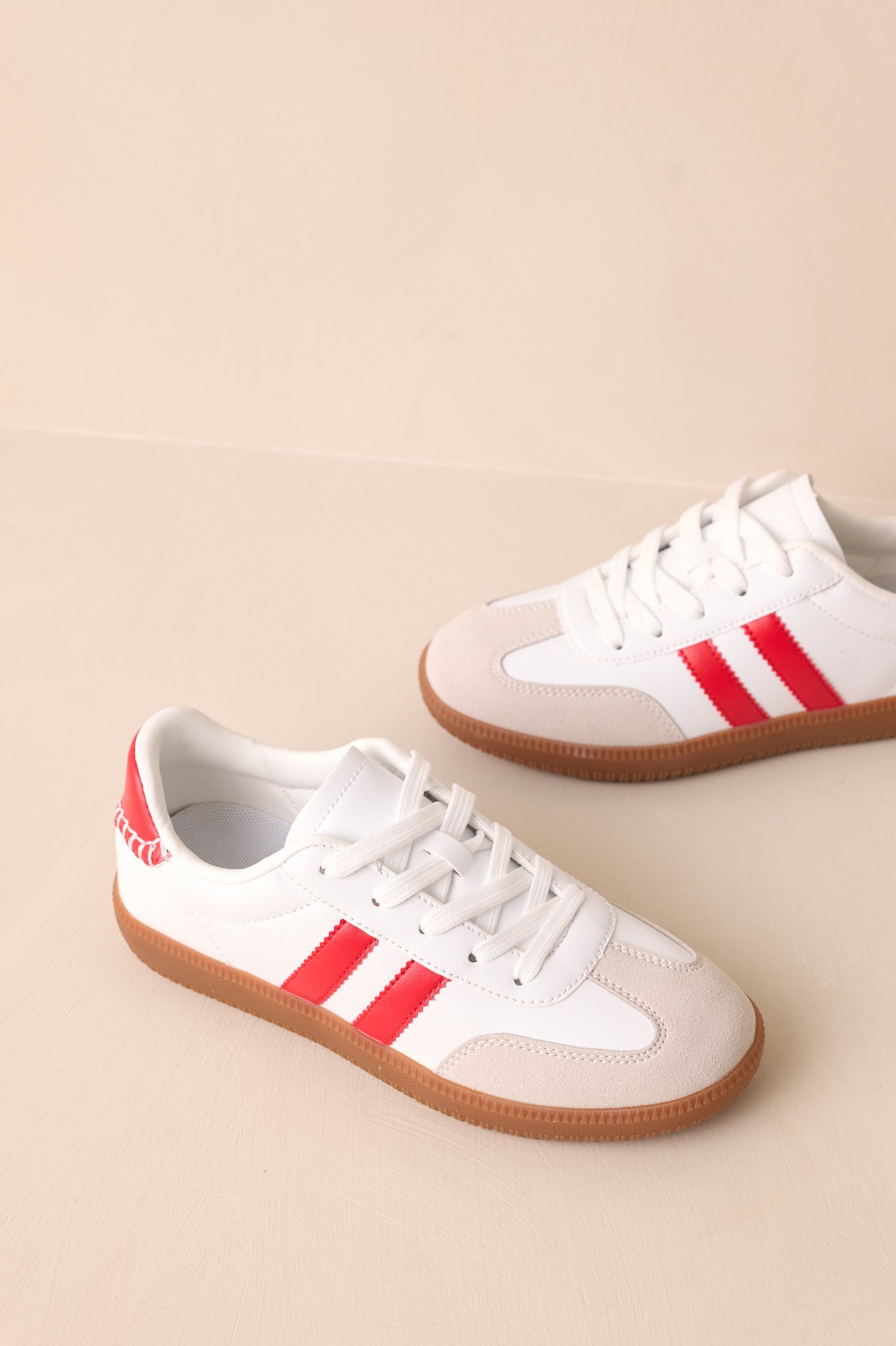 A top-down view highlighting the white laces, round toe, and red faux leather section at the ankle.