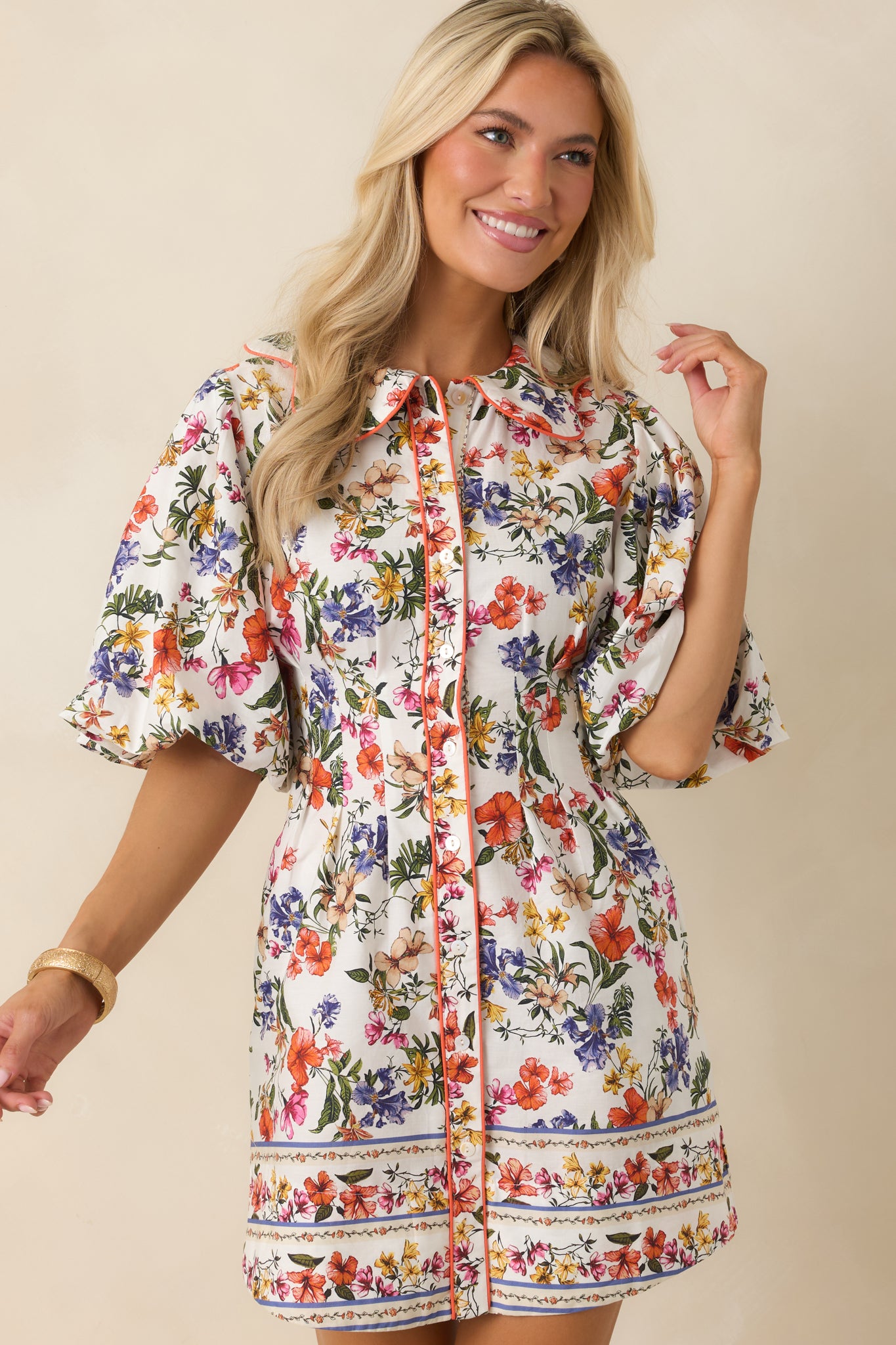 Ivory multi floral mini dress in 100% cotton featuring a colorful floral print, scalloped collar, and contrast orange piping along a functional button-front placket.