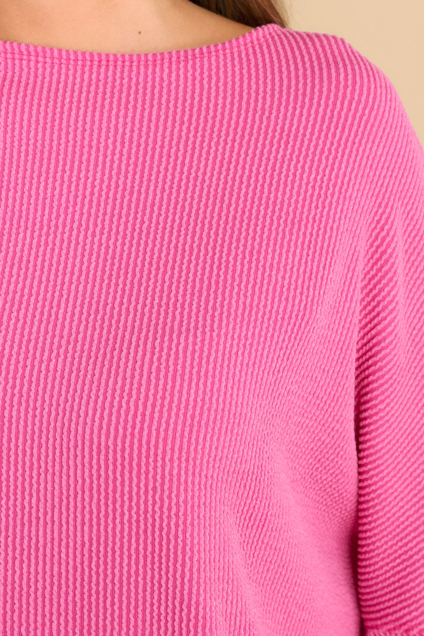 Close up view of this top that features a round neckline, long dolman sleeves, and a slight high low hem line.