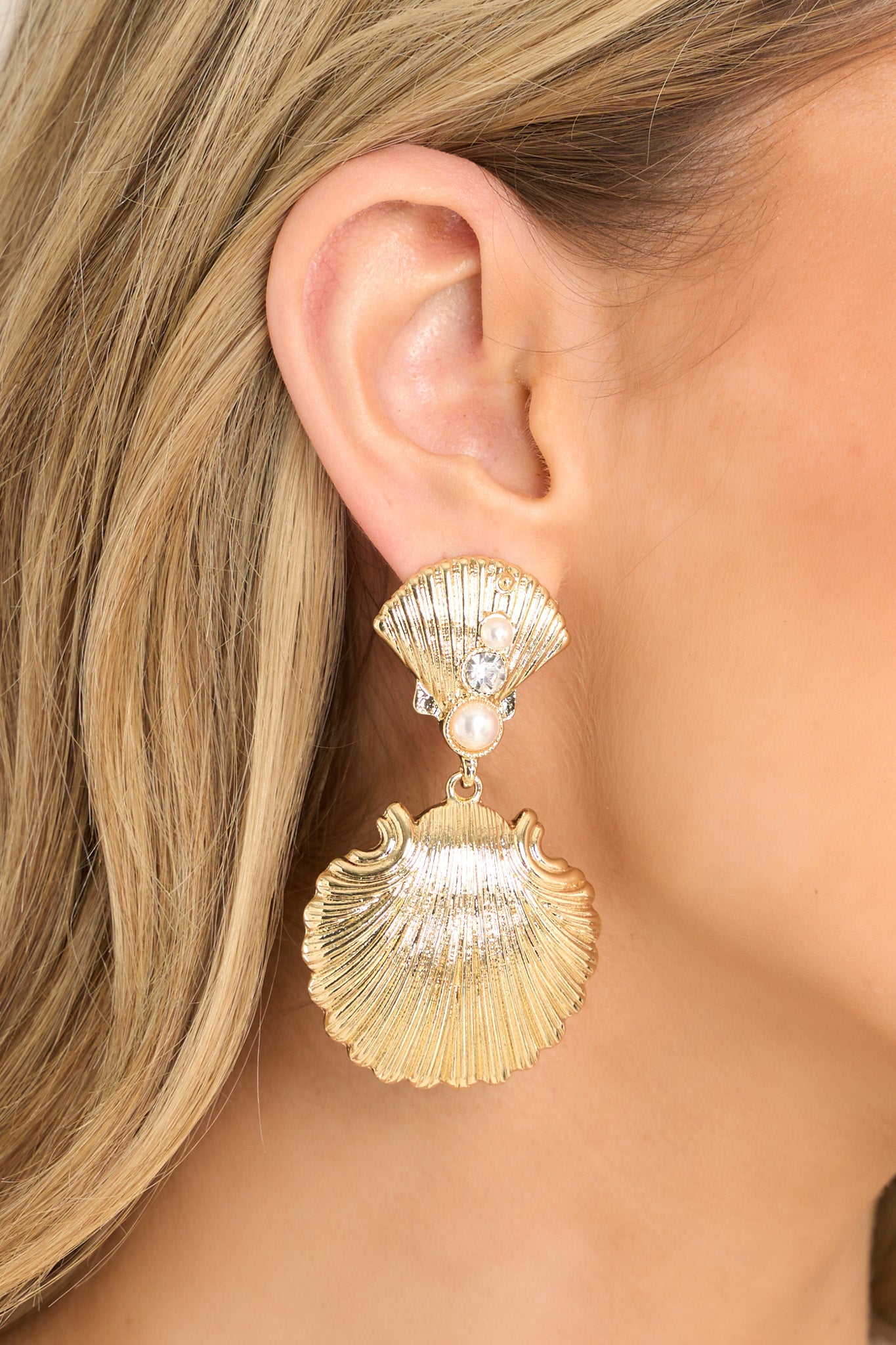 These gold earrings feature gold hardware, a shell shaped stud embellished with faux pearls and rhinestones, a larger shell shaped dangle, and secure post backings.
