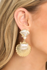These gold earrings feature gold hardware, a shell shaped stud embellished with faux pearls and rhinestones, a larger shell shaped dangle, and secure post backings. 