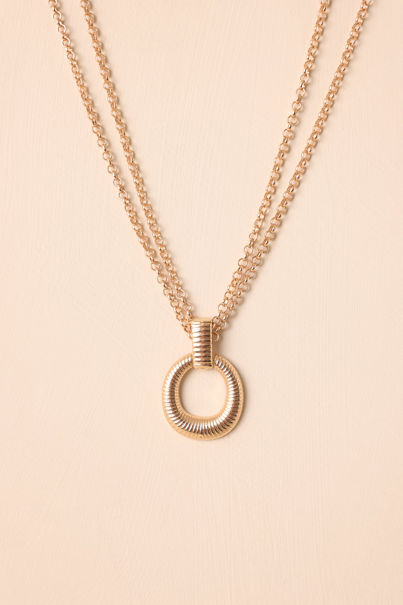 Necklace laid flat on a beige surface, clearly displaying the adjustable double-layered chain and centered round pendant.