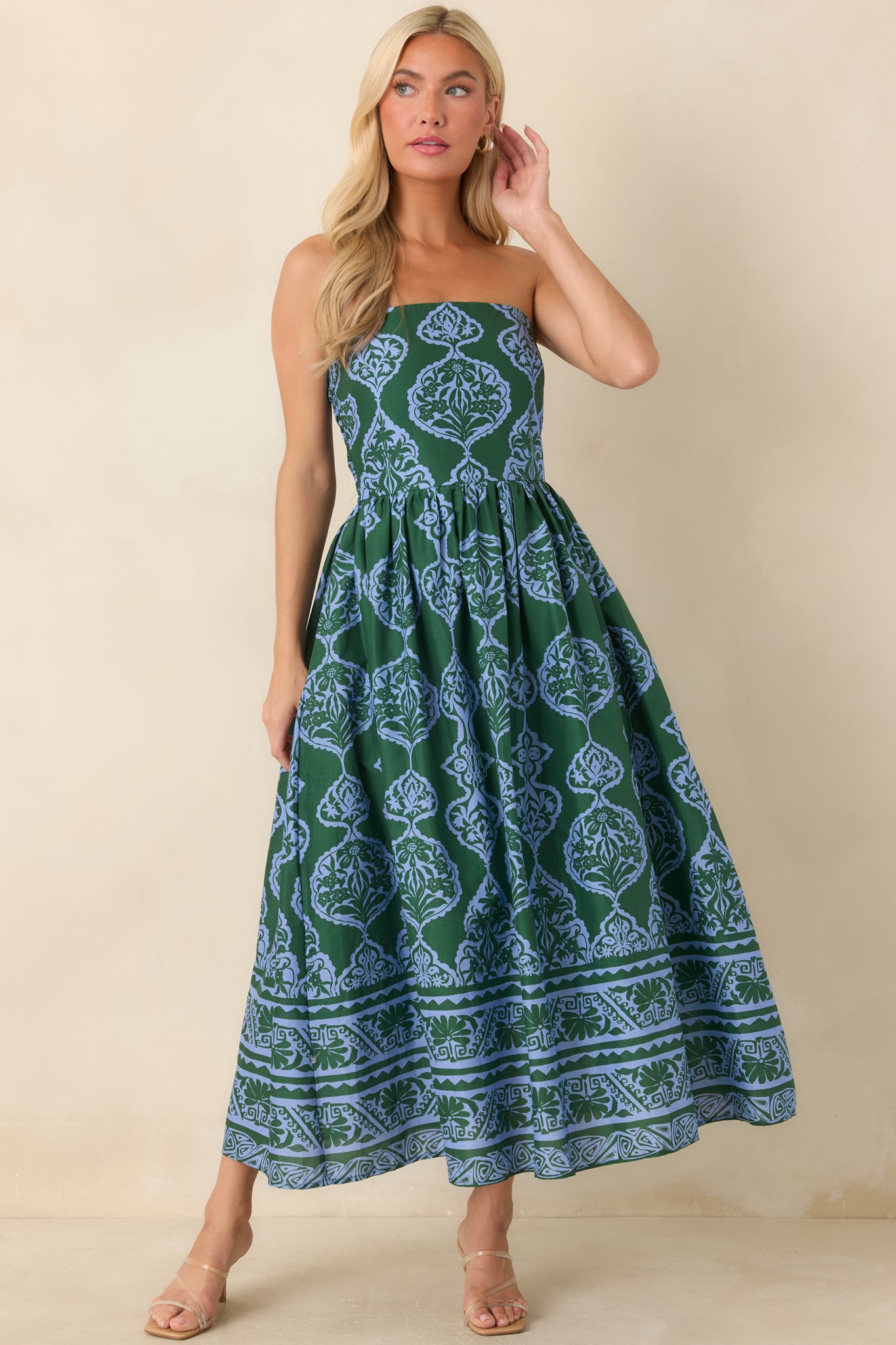 A woman modeling a strapless midi dress with a green and blue paisley block print pattern, standing against a plain beige studio background.