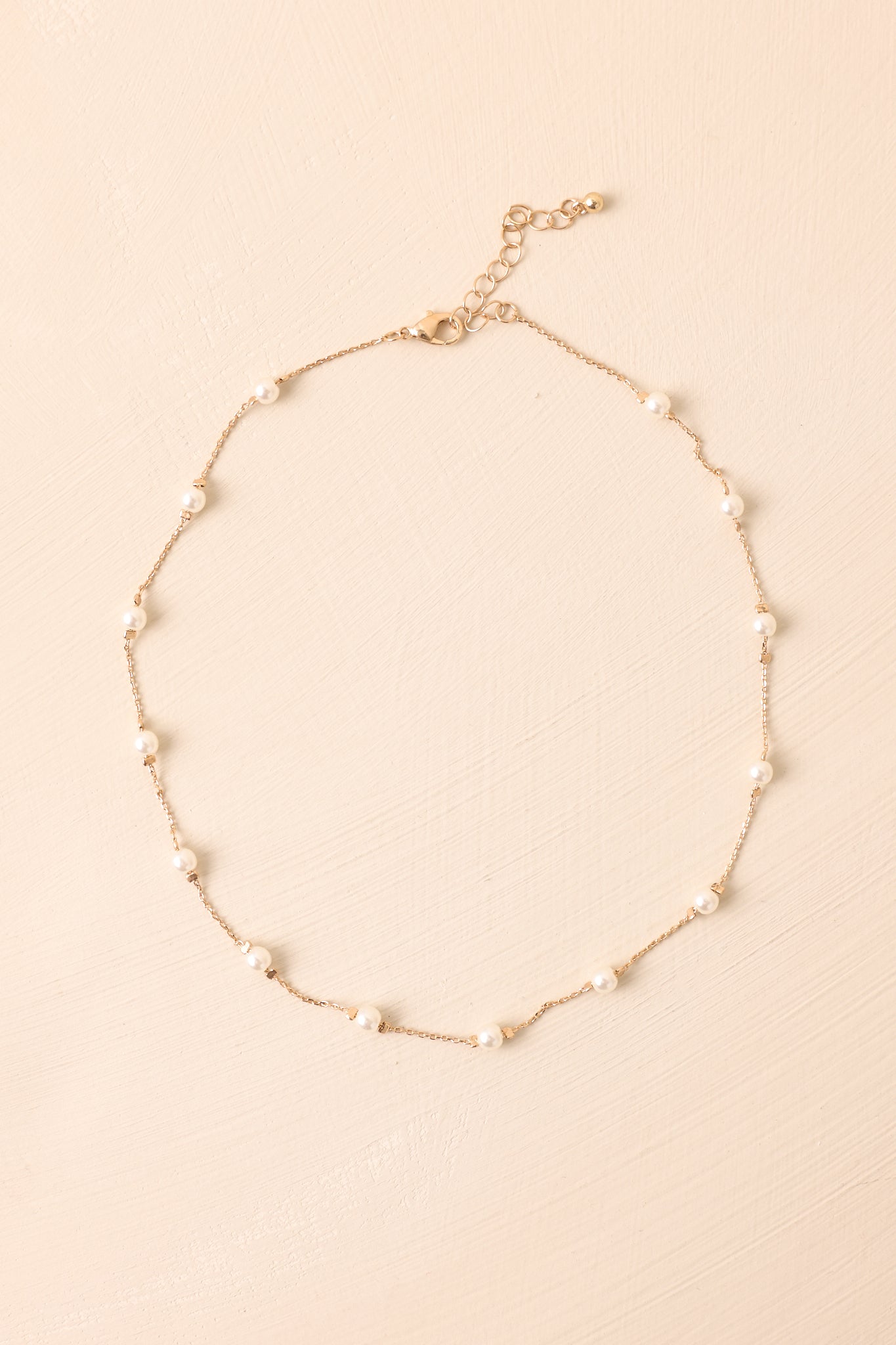 Cropped view of delicate gold-toned chain necklace with evenly spaced faux pearls.