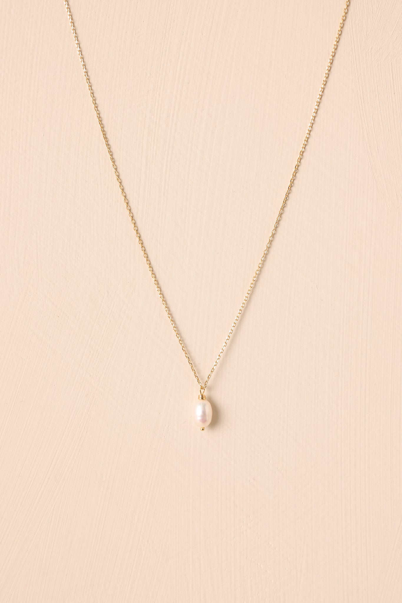 Flat lay of the necklace against a beige background, emphasizing the adjustable length chain and the pearl pendant’s organic shape.