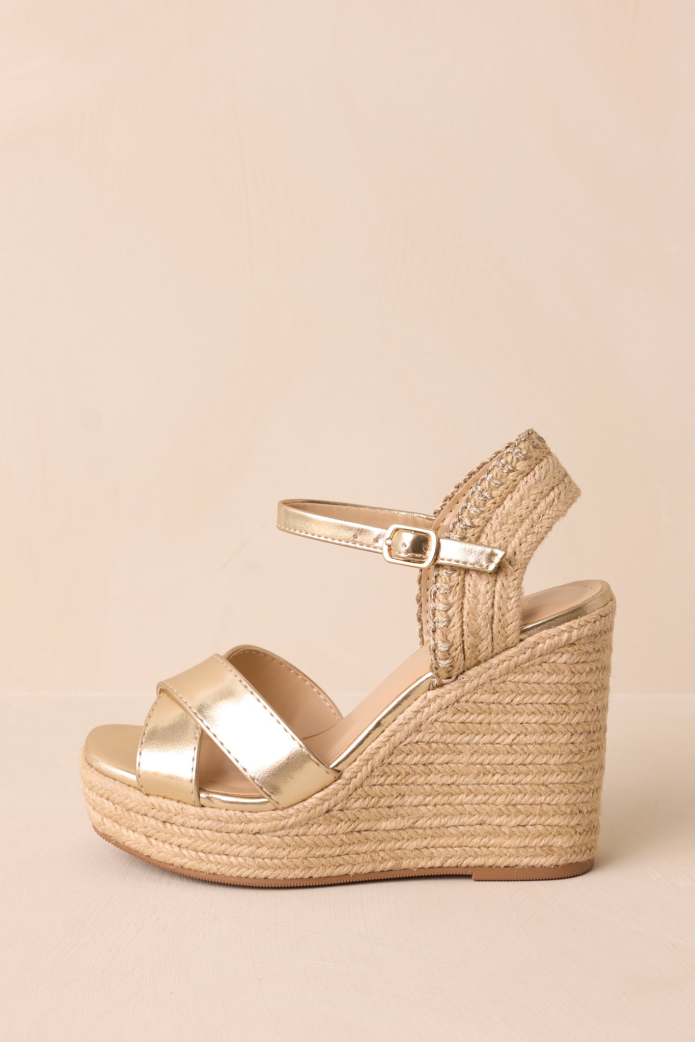 The gold sandals are displayed at a side angle, showing the wedged heel, platform bottom, and cross straps over the foot with a clear view of the adjustable ankle strap.