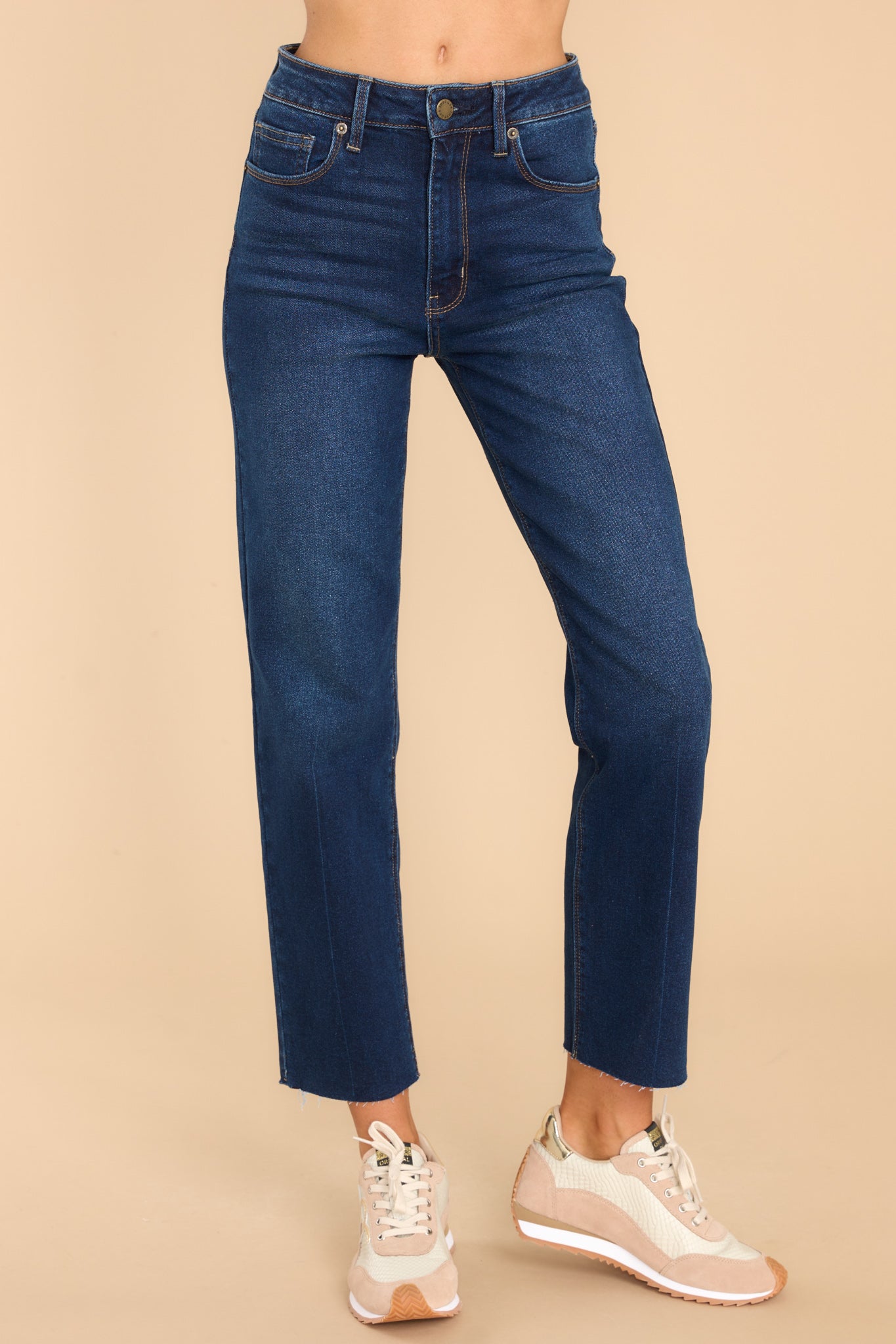 These dark wash denim jeans feature a zipper down the front with one button closure, five functional pockets, a straight leg and a raw hem at the bottom.