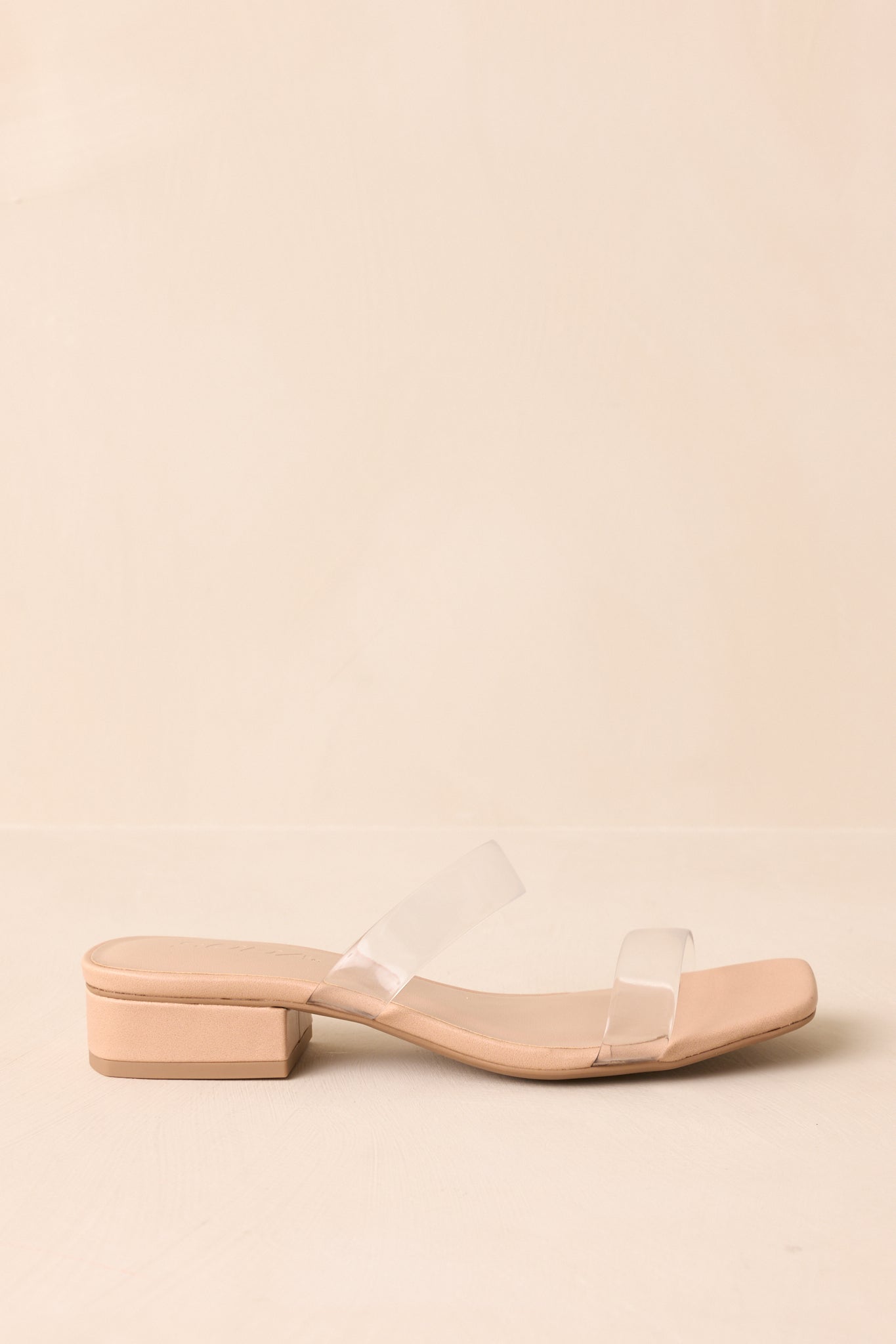 Side profile of clear strap heels with short block heel on beige background.