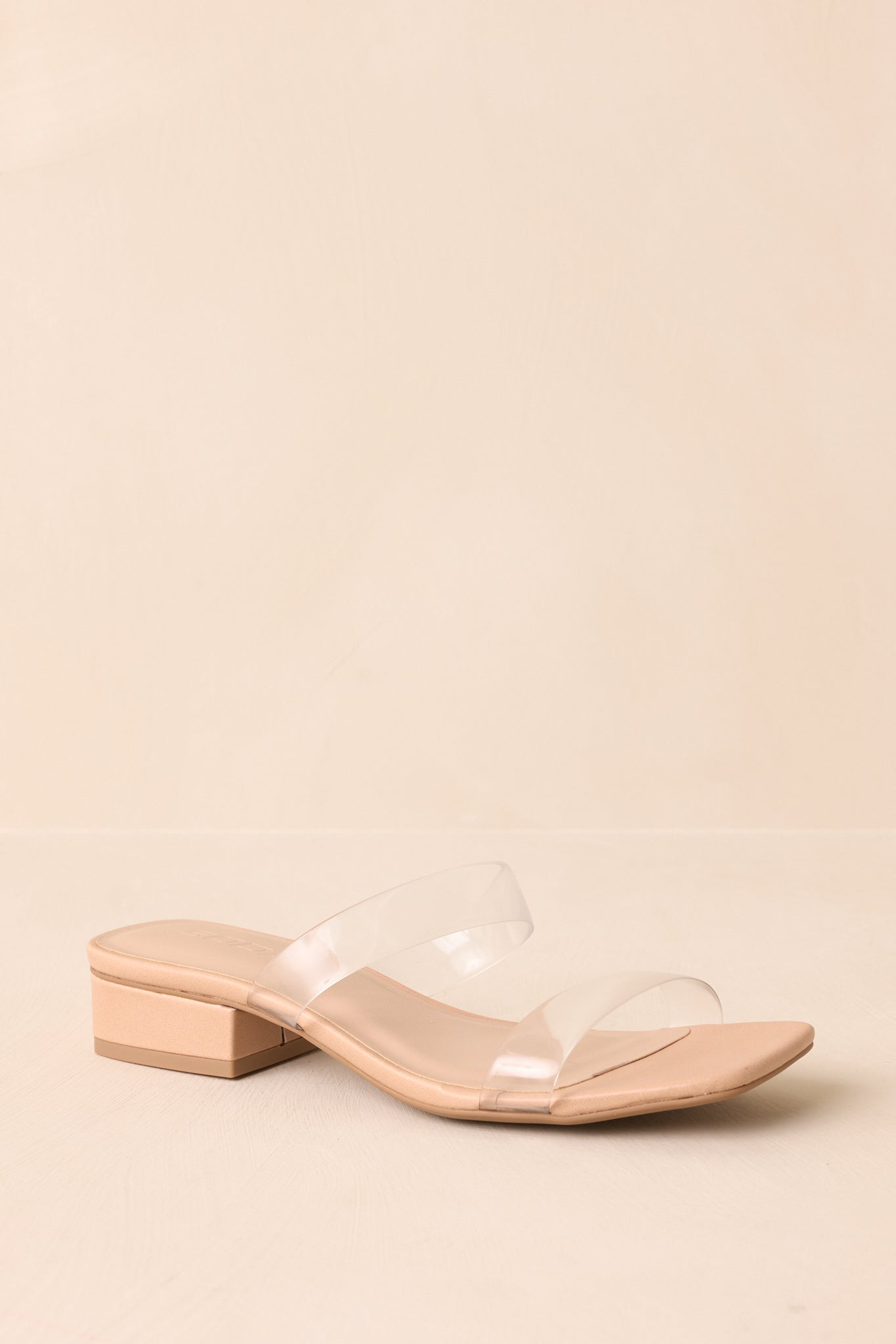 Slide-on heels with clear straps displayed on beige backdrop at a forward angle.