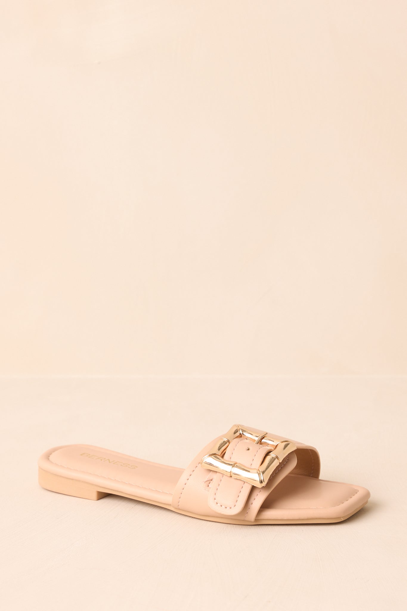 Beige faux leather sandals displayed on beige backdrop at an angle.