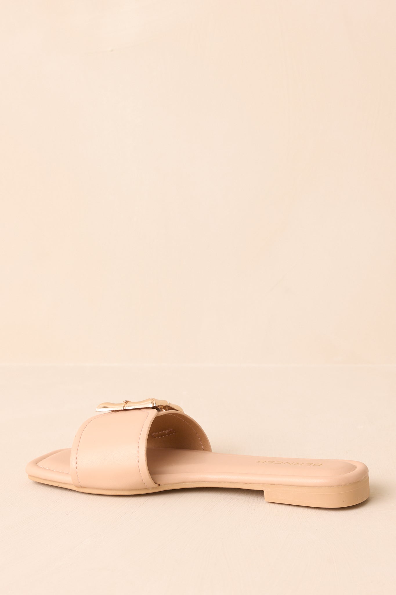 Low-angle view of beige faux leather sandals showing slip-on style.