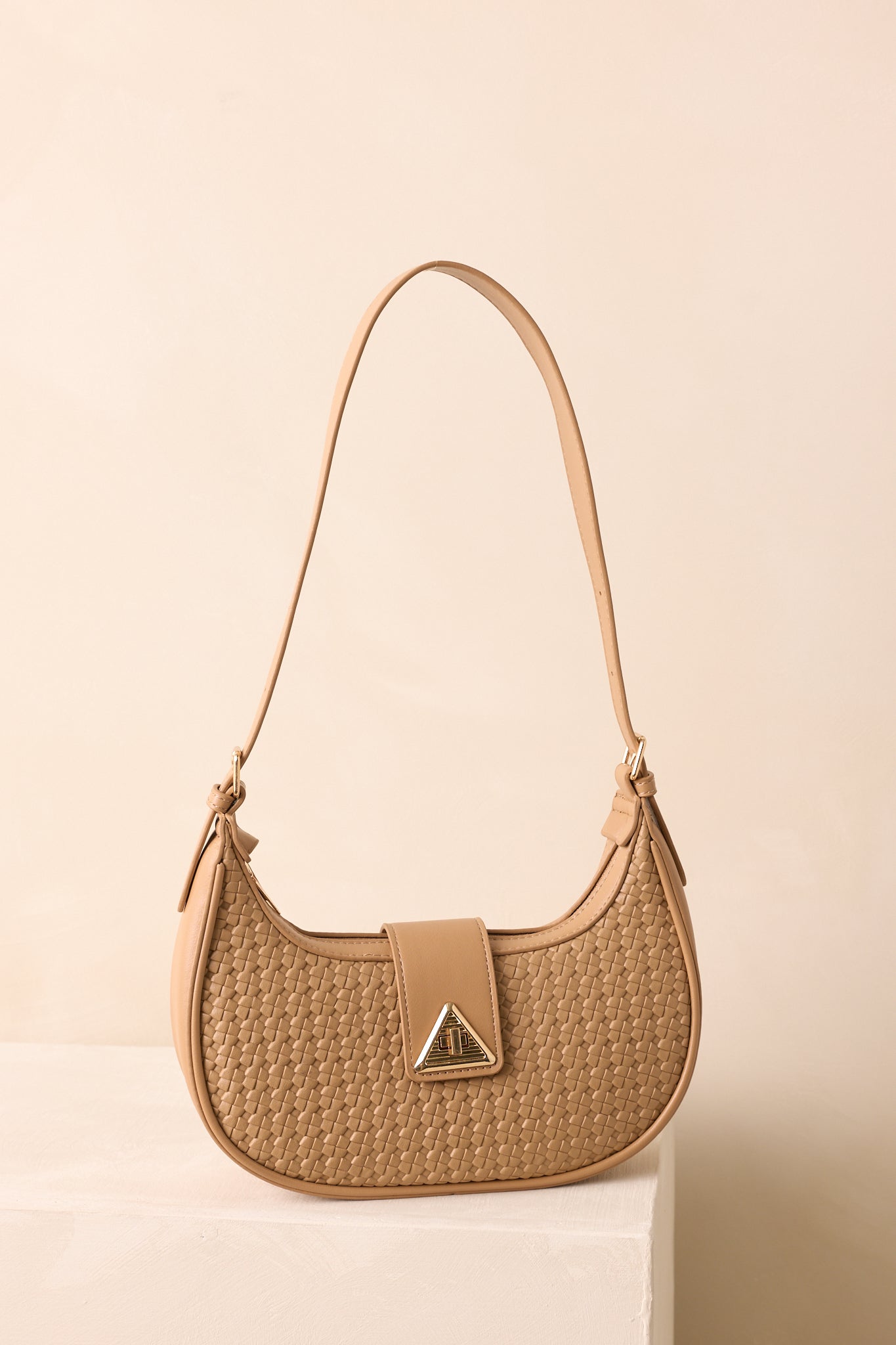 A full front view of the beige half-moon shoulder bag with a woven faux leather design and gold twist-lock flap closure.