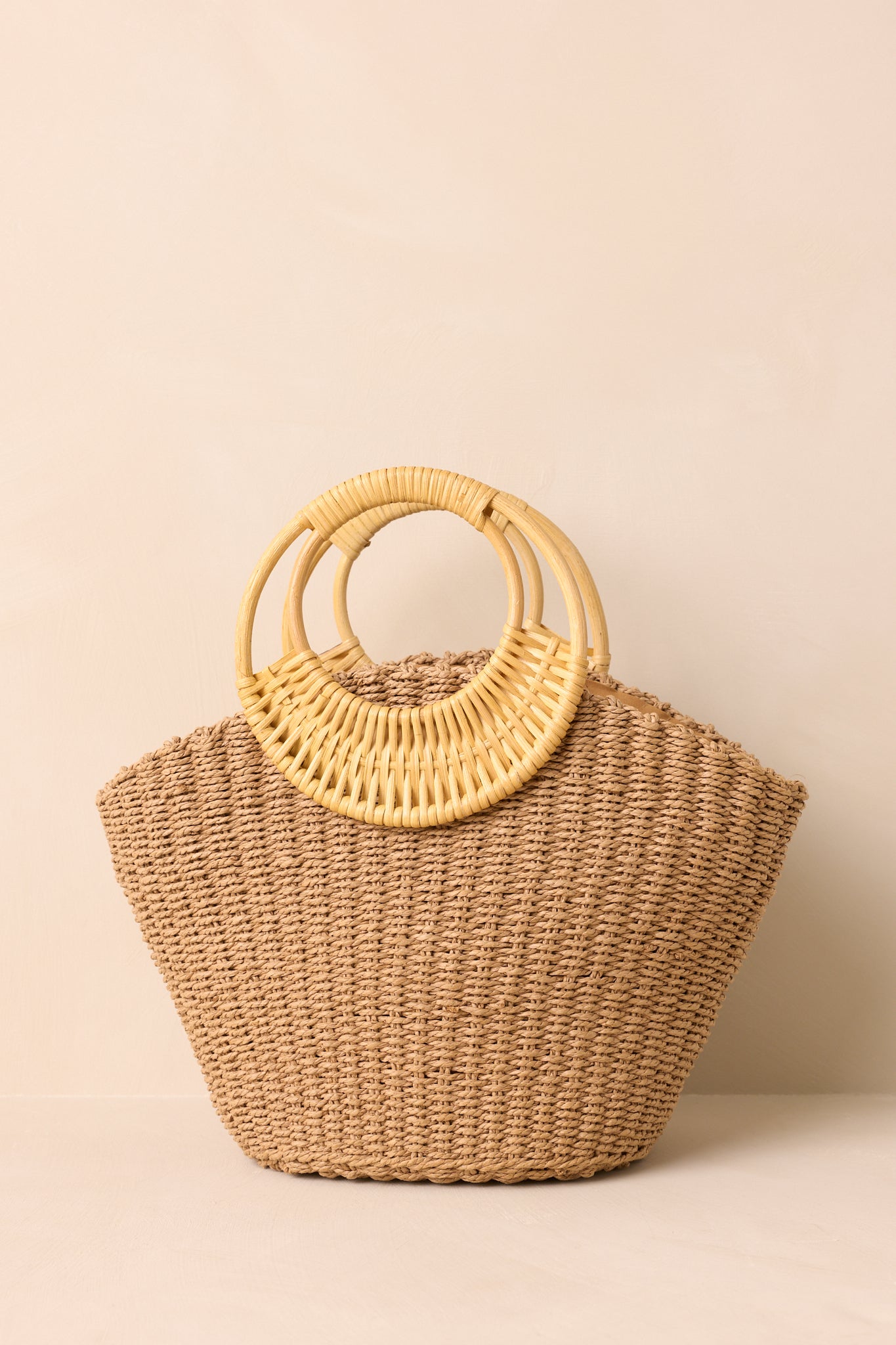 Close view of tan raffia weave and smooth bamboo handles on handbag.