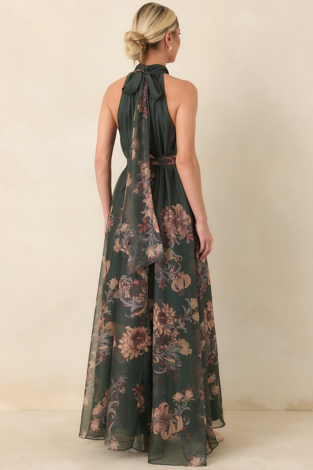 Rear view of the forest green maxi dress showing the halter ties with long flowing ends, back keyhole, and sheer floral skirt overlay.